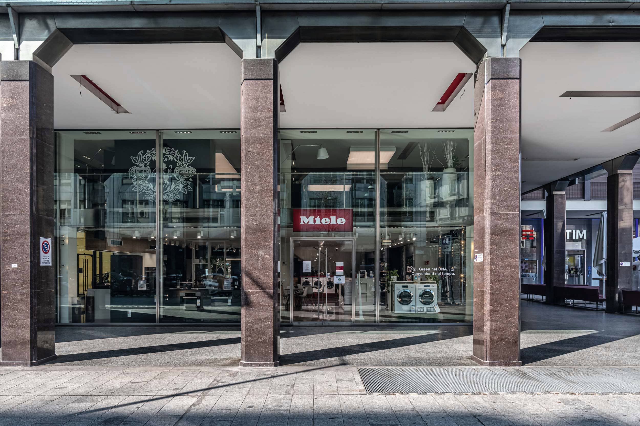Vista a livello strada di uno showroom Miele con facciata in vetro, colonne e lavatrici in esposizione.