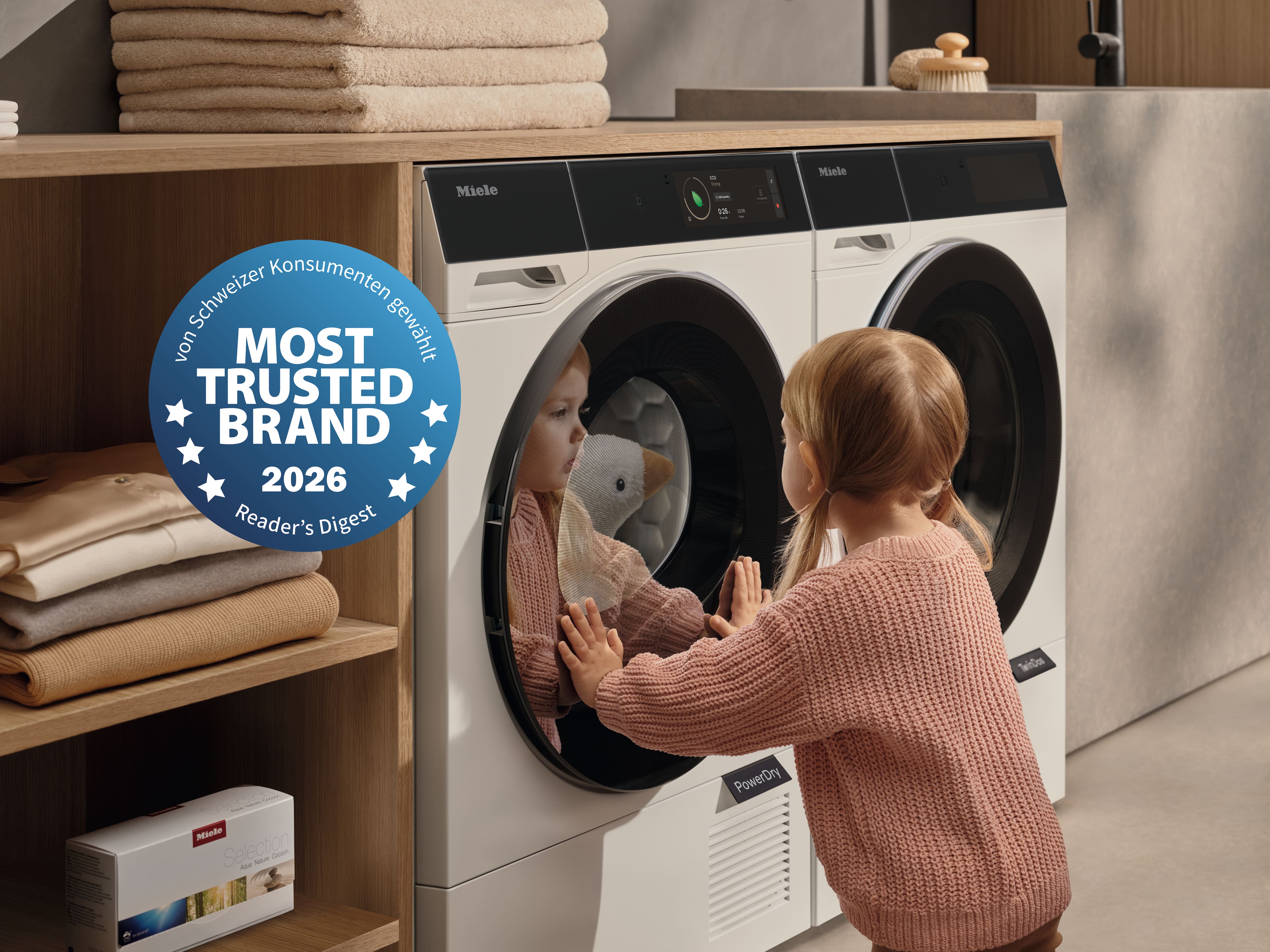 Bild mit Mädchen in einem rosa Pullover. Sie schaut ihrem Plüschtier in der Waschmaschine zu. Daneben das Siegel vom "Most Trusted Brand 2026"
