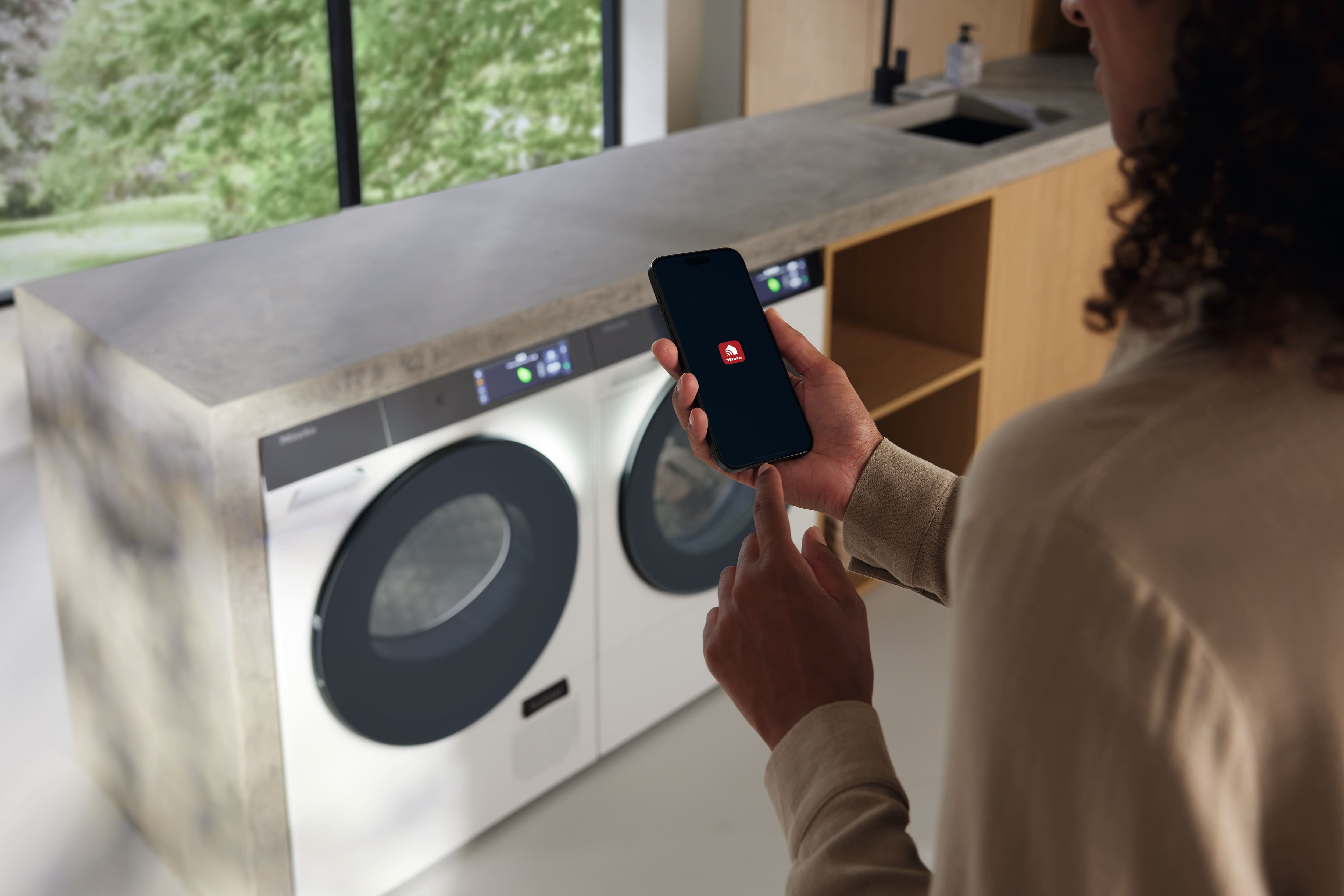 Persona che utilizza uno smartphone per controllare una lavatrice e asciugatrice moderna in una lavanderia elegante. Persona che utilizza uno smartphone per controllare una lavatrice e asciugatrice moderna in una lavanderia elegante.
