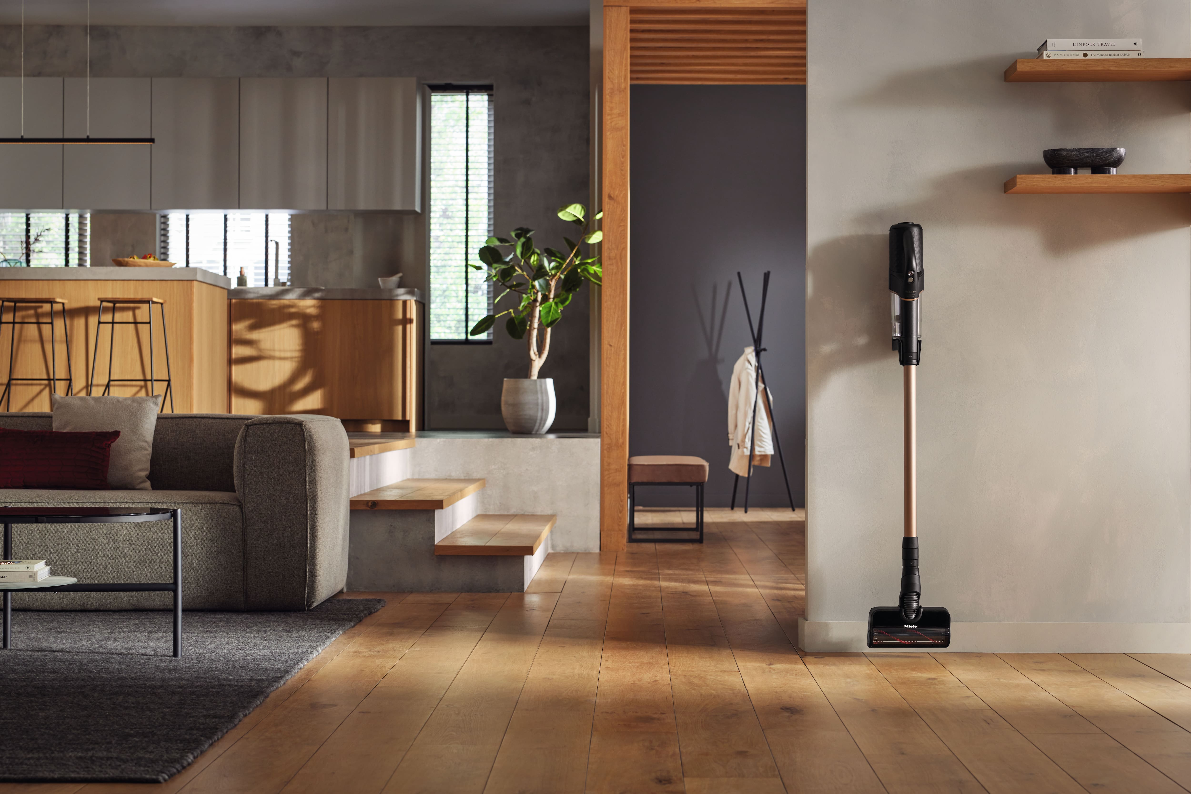Zeitgenössischer, offener Wohnbereich mit Holzböden, einem grauen Sofa und einem kabellosen Staubsauger, der an der Wand steht. Zeitgenössischer, offener Wohnbereich mit Holzböden, einem grauen Sofa und einem kabellosen Staubsauger, der an der Wand steht.