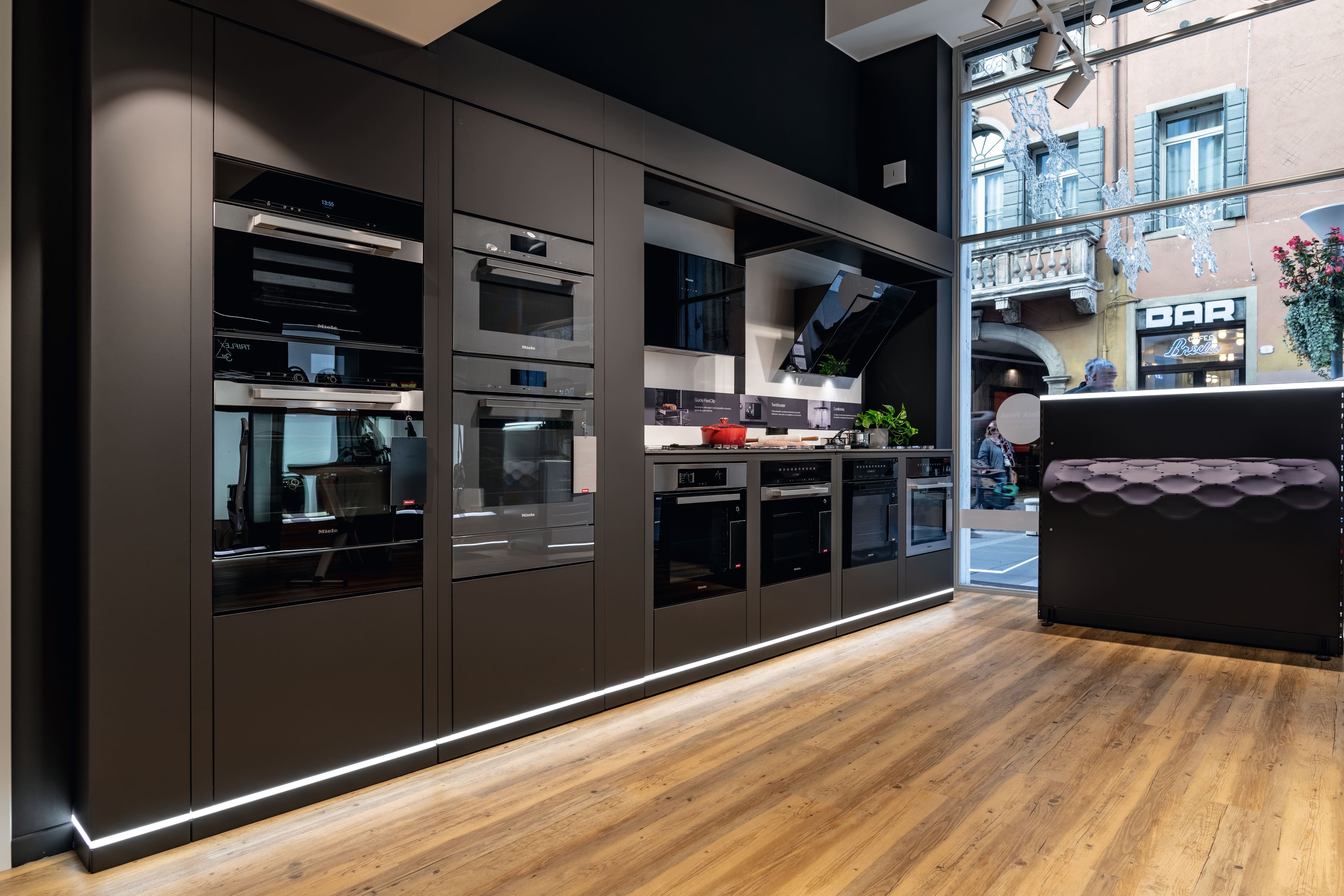 Showroom di cucine moderne con mobili neri opachi, forni incassati, cappa e pavimenti in legno vicino alla finestra sulla strada. Showroom di cucine moderne con mobili neri opachi, forni incassati, cappa e pavimenti in legno vicino alla finestra sulla strada.