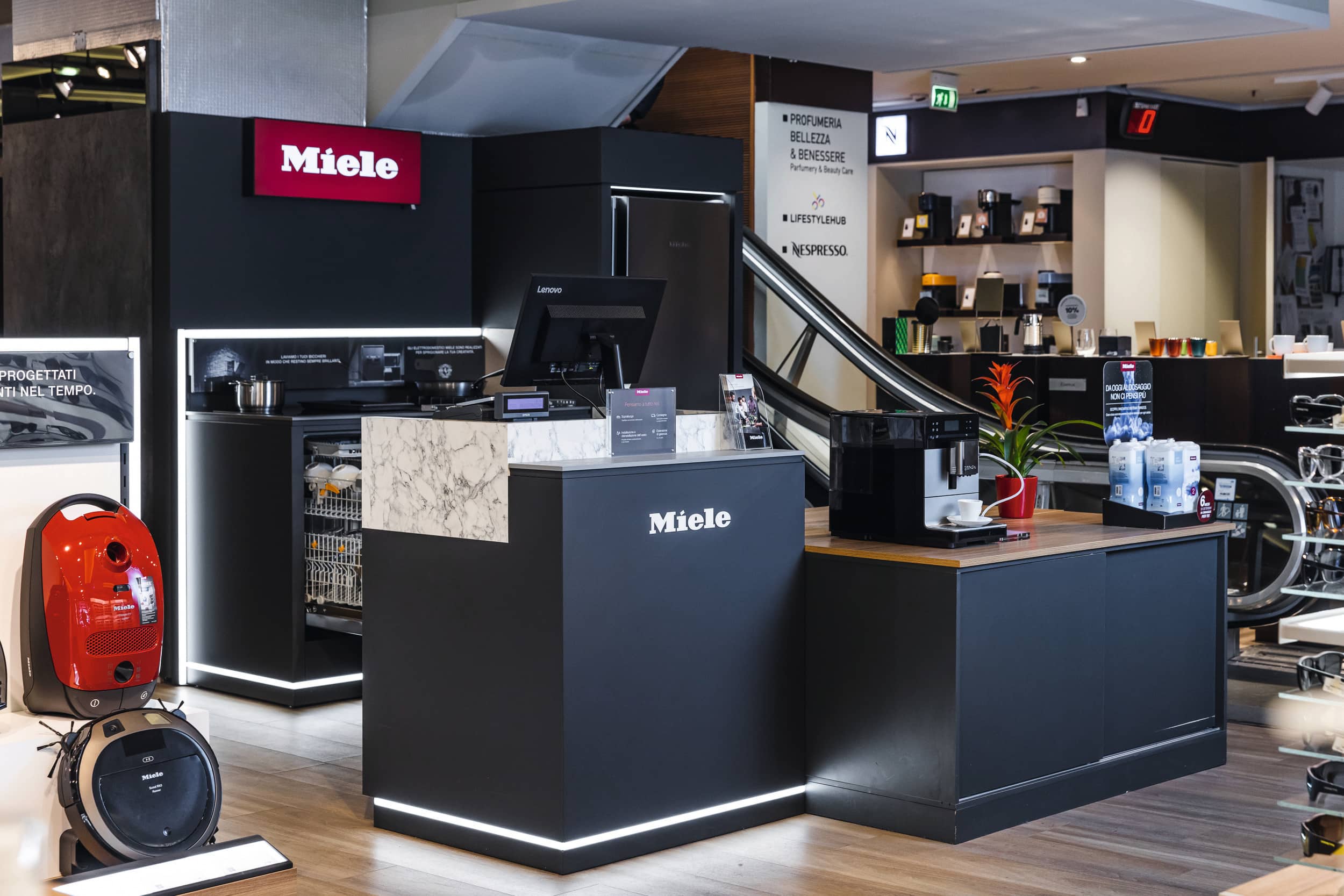 Esposizione al dettaglio Miele con elettrodomestici dimostrativi—macchina da caffè, lavastoviglie e aspirapolvere—al bancone di uno showroom moderno. Esposizione al dettaglio Miele con elettrodomestici dimostrativi—macchina da caffè, lavastoviglie e aspirapolvere—al bancone di uno showroom moderno.