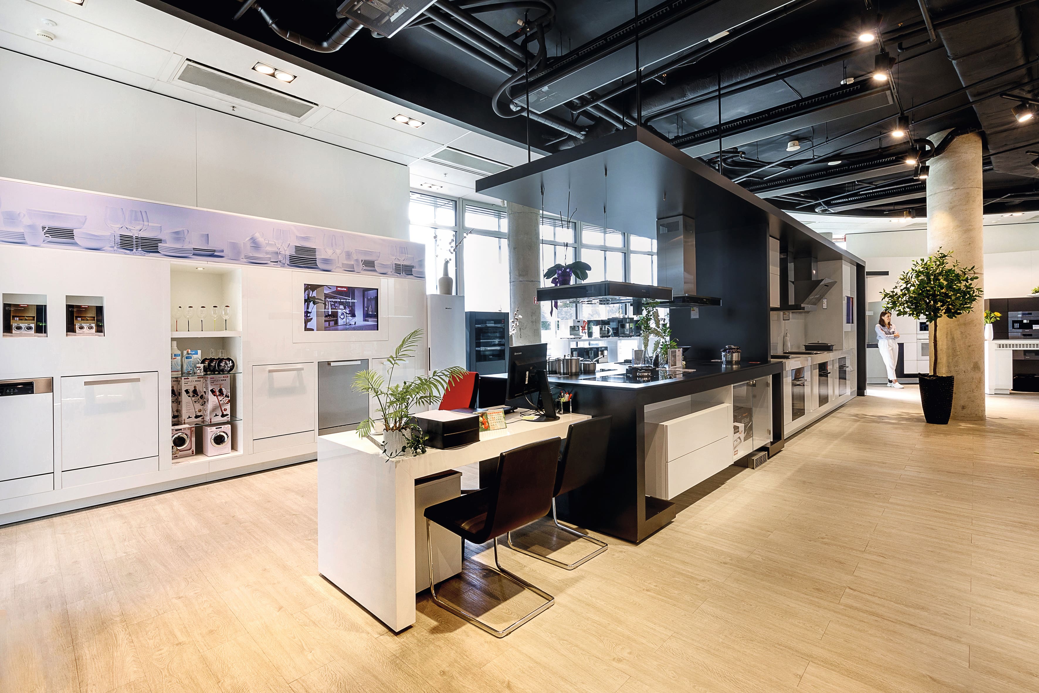 Moderni virtuvės ekspozicija su elegantiškais prietaisais, centrine sala ir atvirais lubų ortakiais po ryškiu apšvietimu. Moderni virtuvės ekspozicija su elegantiškais prietaisais, centrine sala ir atvirais lubų ortakiais po ryškiu apšvietimu.