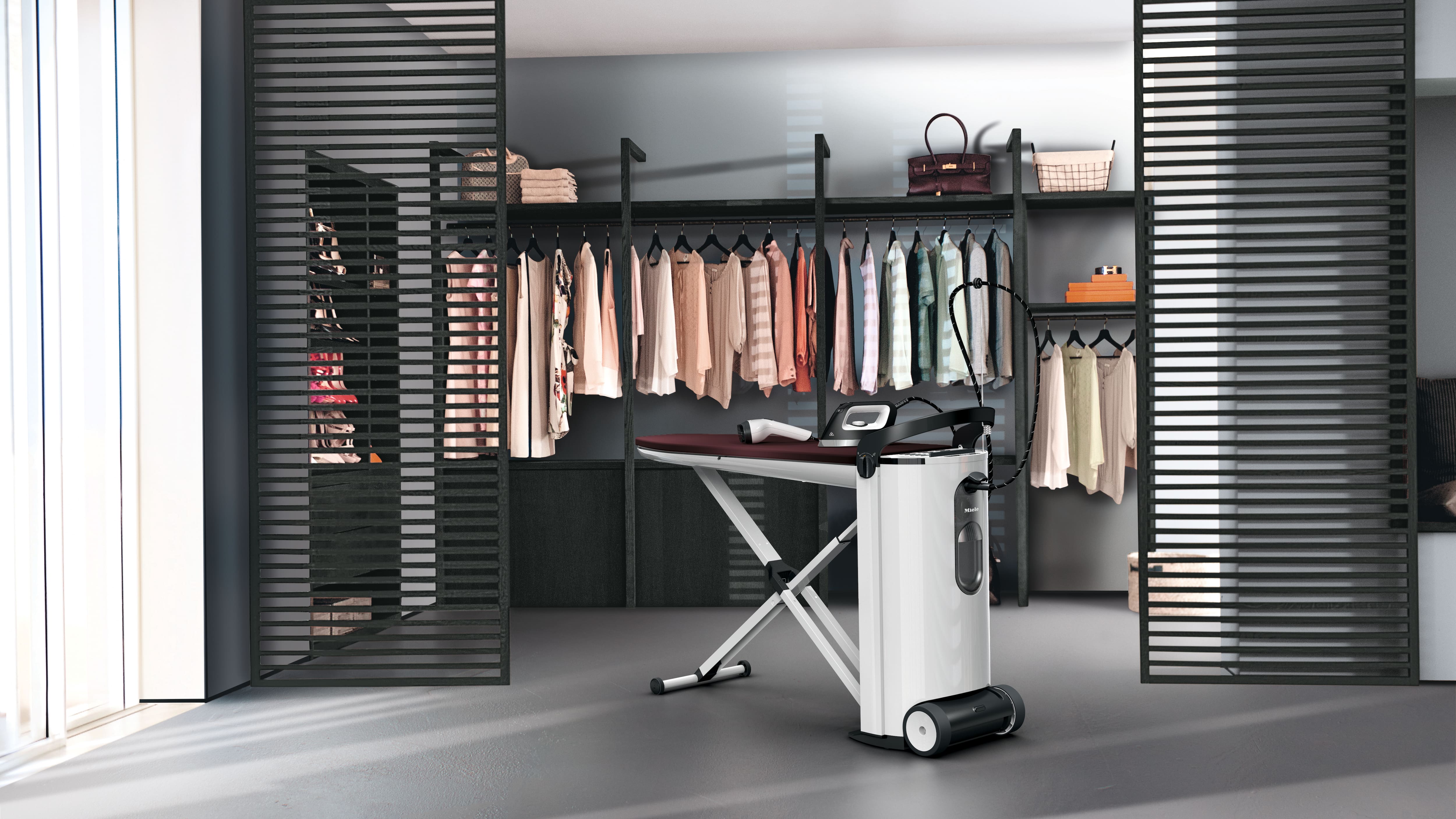Moderner begehbarer Kleiderschrank mit hängender Kleidung und Regalen, im Vordergrund eine High-Tech-Dampfbügelstation. Moderner begehbarer Kleiderschrank mit hängender Kleidung und Regalen, im Vordergrund eine High-Tech-Dampfbügelstation.