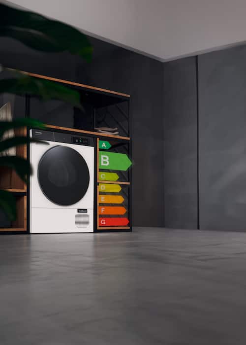 Moderne fellesvaskeri med Mieles tørketrommel med front utensiler ved siden av fargerike A-G-energiklassifiseringstabeller som fremhever B.