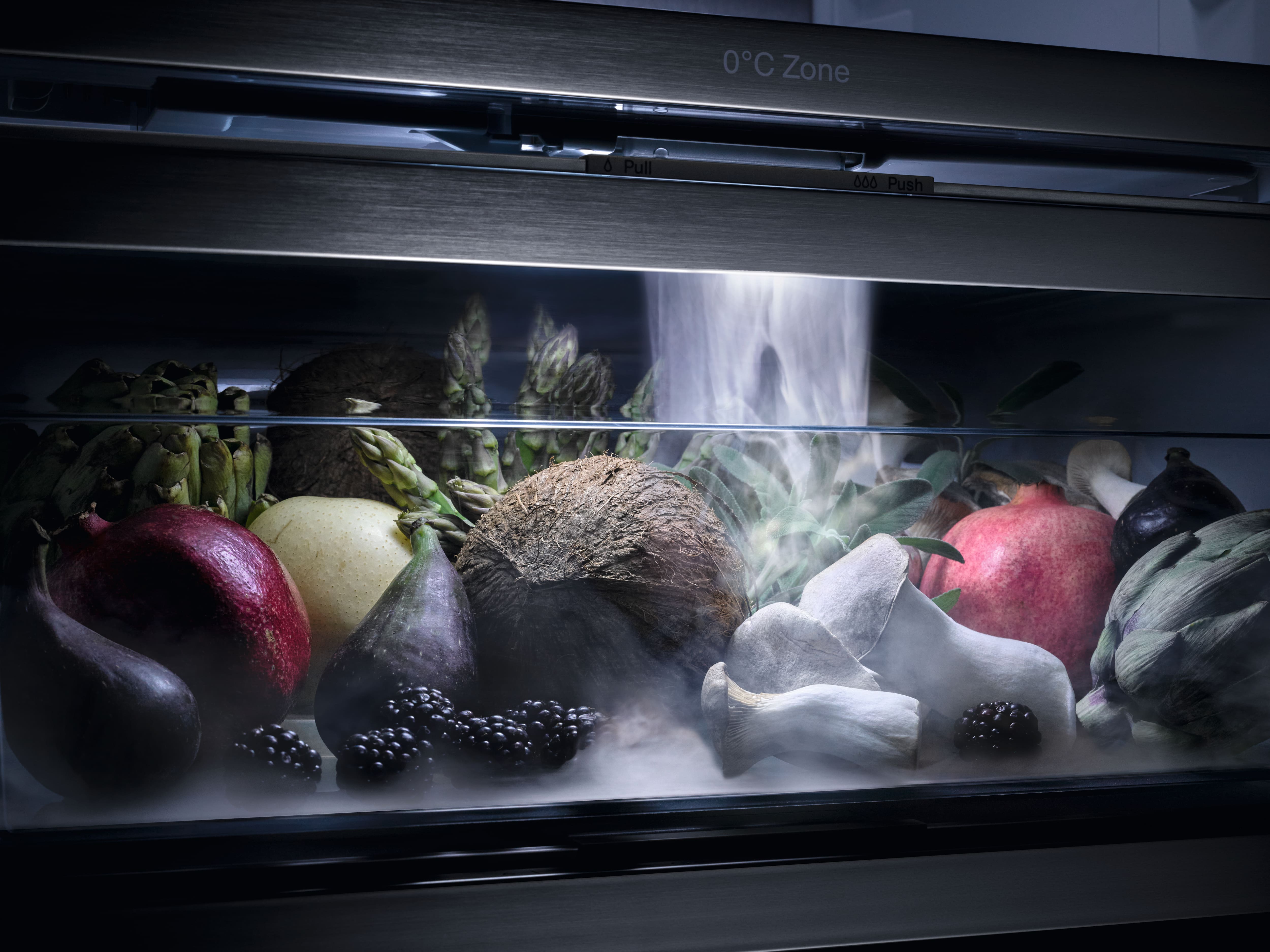 Un assortiment de fruits et légumes dans un bac réfrigéré à 0 °C, de la brume tourbillonnant autour des grenades, des noix de coco, des figues, des artichauts et des champignons.