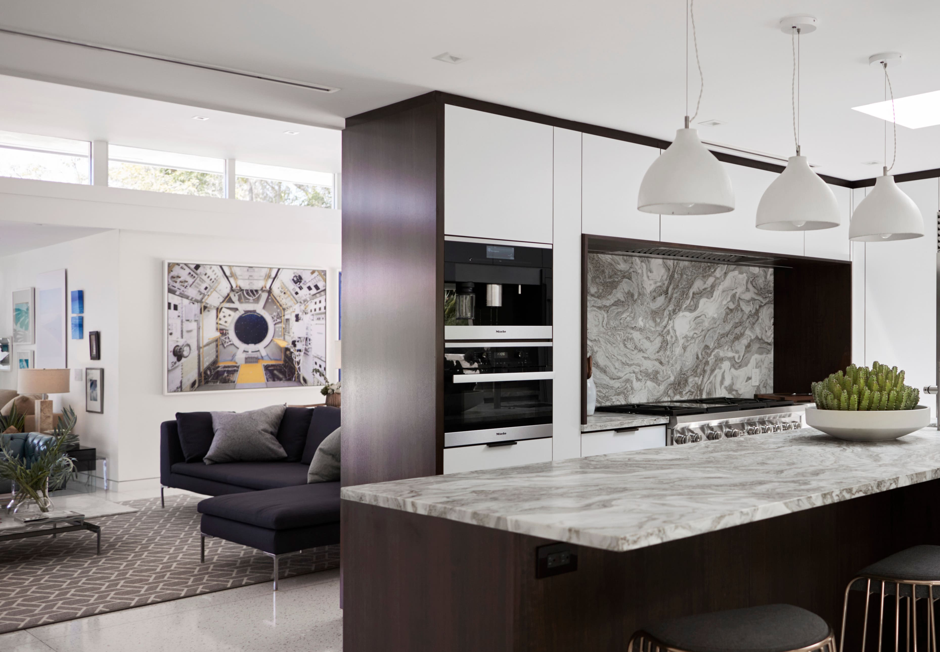 Modern open-plan kitchen with marble island, pendant lights, sleek cabinetry, and adjacent lounge area. Modern open-plan kitchen with marble island, pendant lights, sleek cabinetry, and adjacent lounge area.