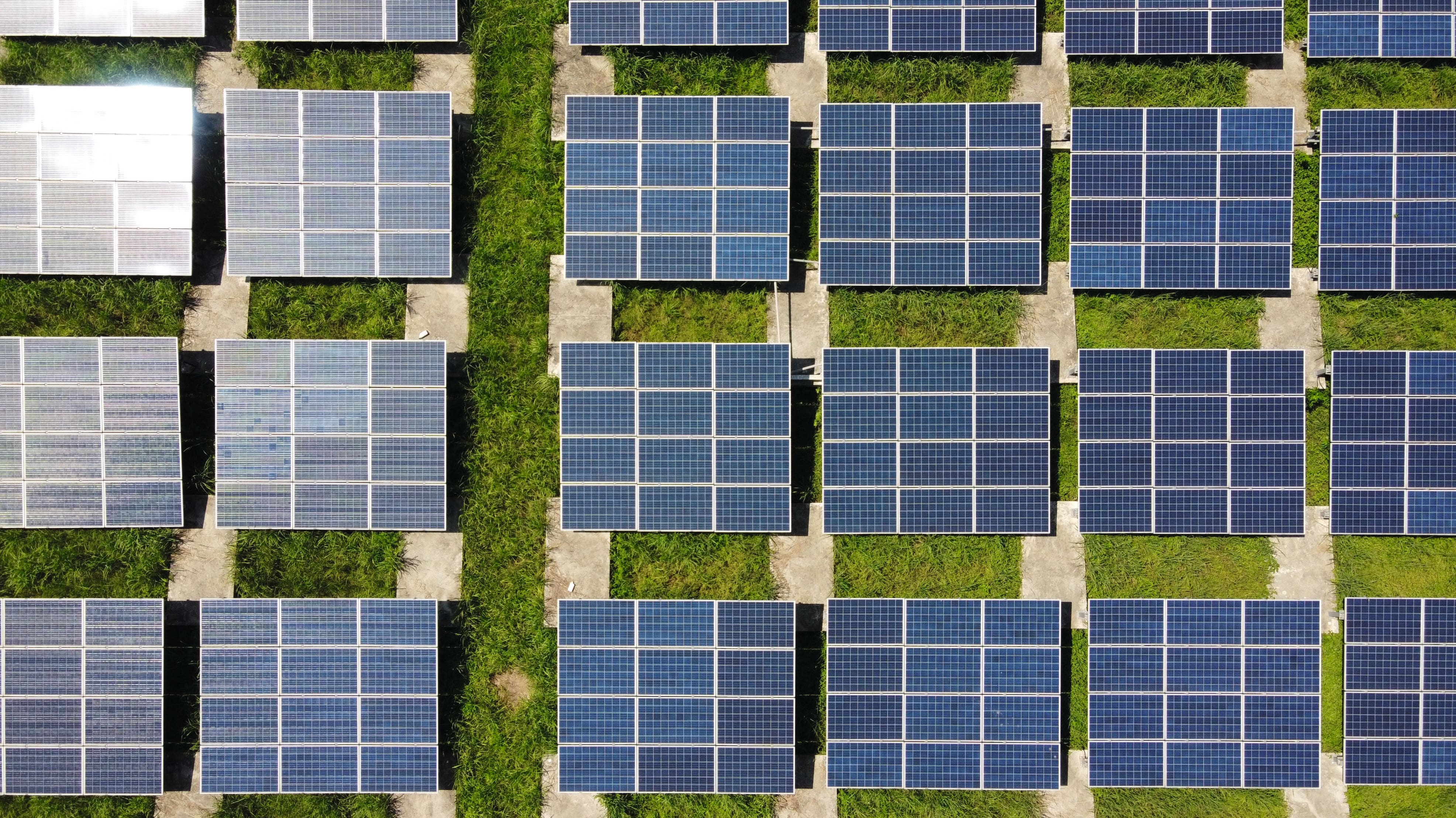 Luftaufnahme eines Solarparks mit Reihen blauer Photovoltaikmodule auf einer Wiesenfläche zur Erzeugung erneuerbarer Energie.