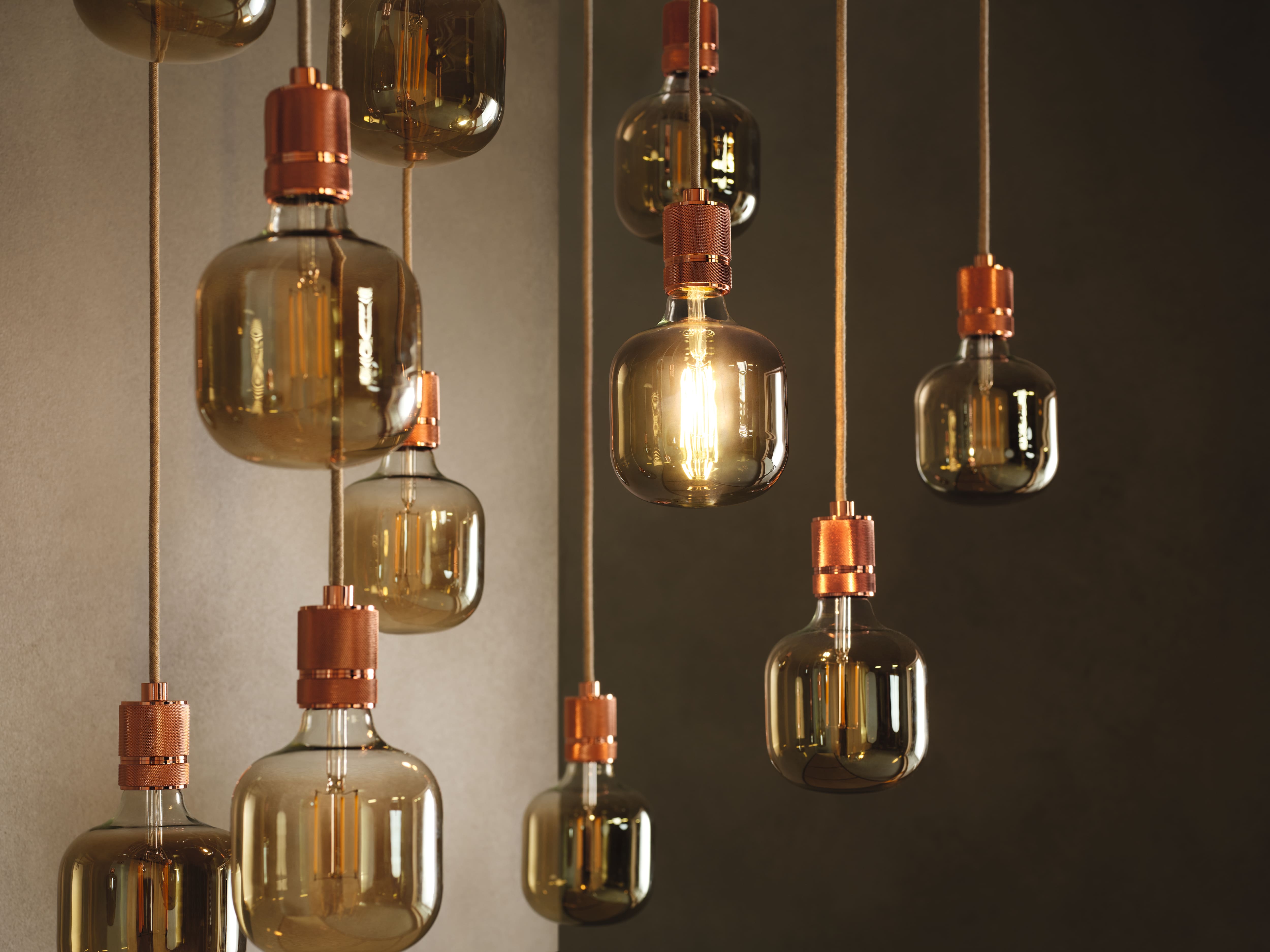Cluster van vintage-stijl hanglampen met amberkleurig glas en koperen fittingen, één gloeilamp gloeit warm. Cluster van vintage-stijl hanglampen met amberkleurig glas en koperen fittingen, één gloeilamp gloeit warm.