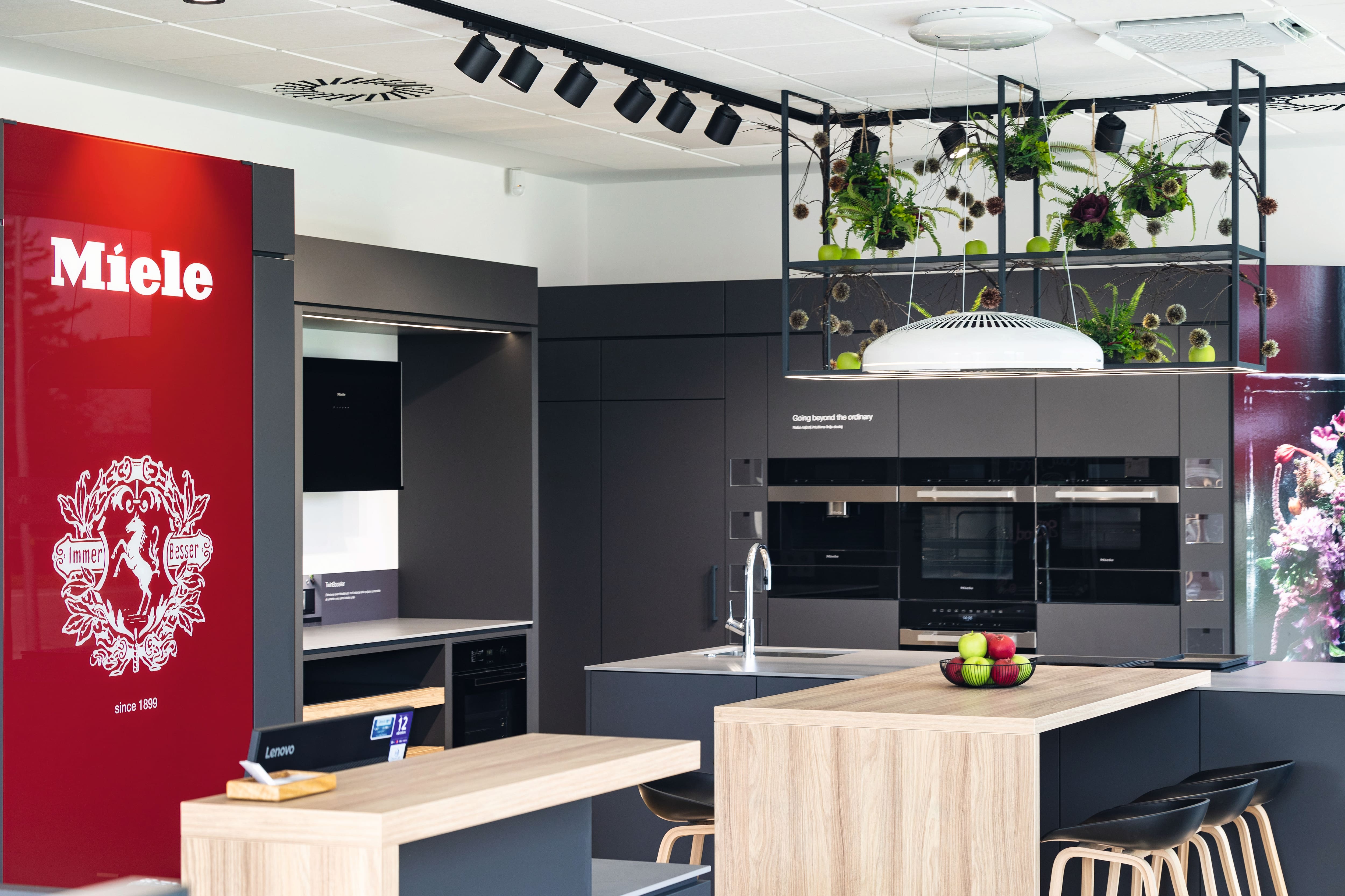 Moderna kuhinja s showroomom z Miele blagovno znamko, vgrajenimi pečicami in otokom, poudarja vrhunske aparate in dizajn.