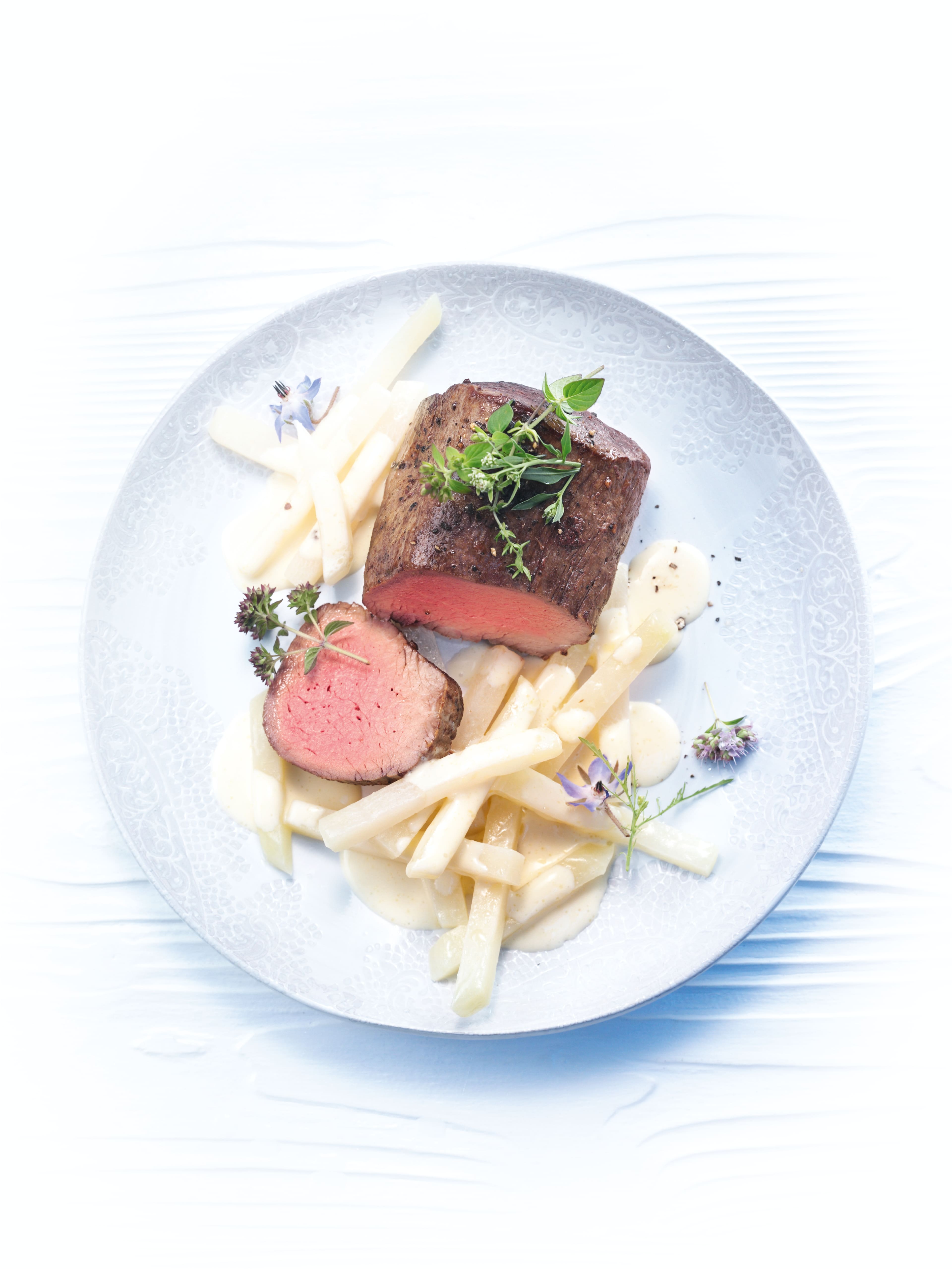 Plated beef tenderloin, sliced and medium-rare, with white asparagus in creamy sauce, herb and flower garnish. Plated beef tenderloin, sliced and medium-rare, with white asparagus in creamy sauce, herb and flower garnish.