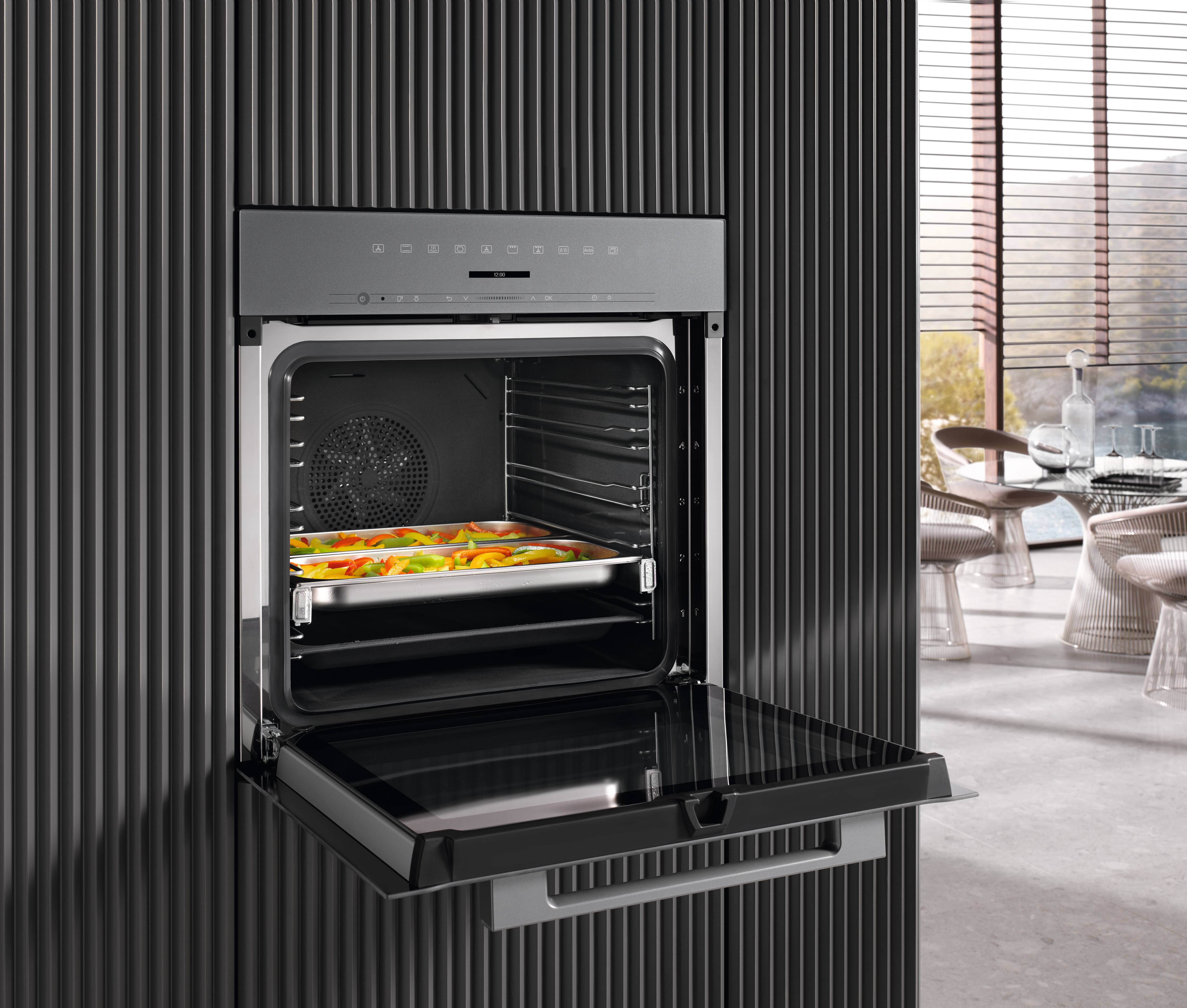 Um forno Miele aberto com vegetais dentro Um forno Miele aberto com vegetais dentro