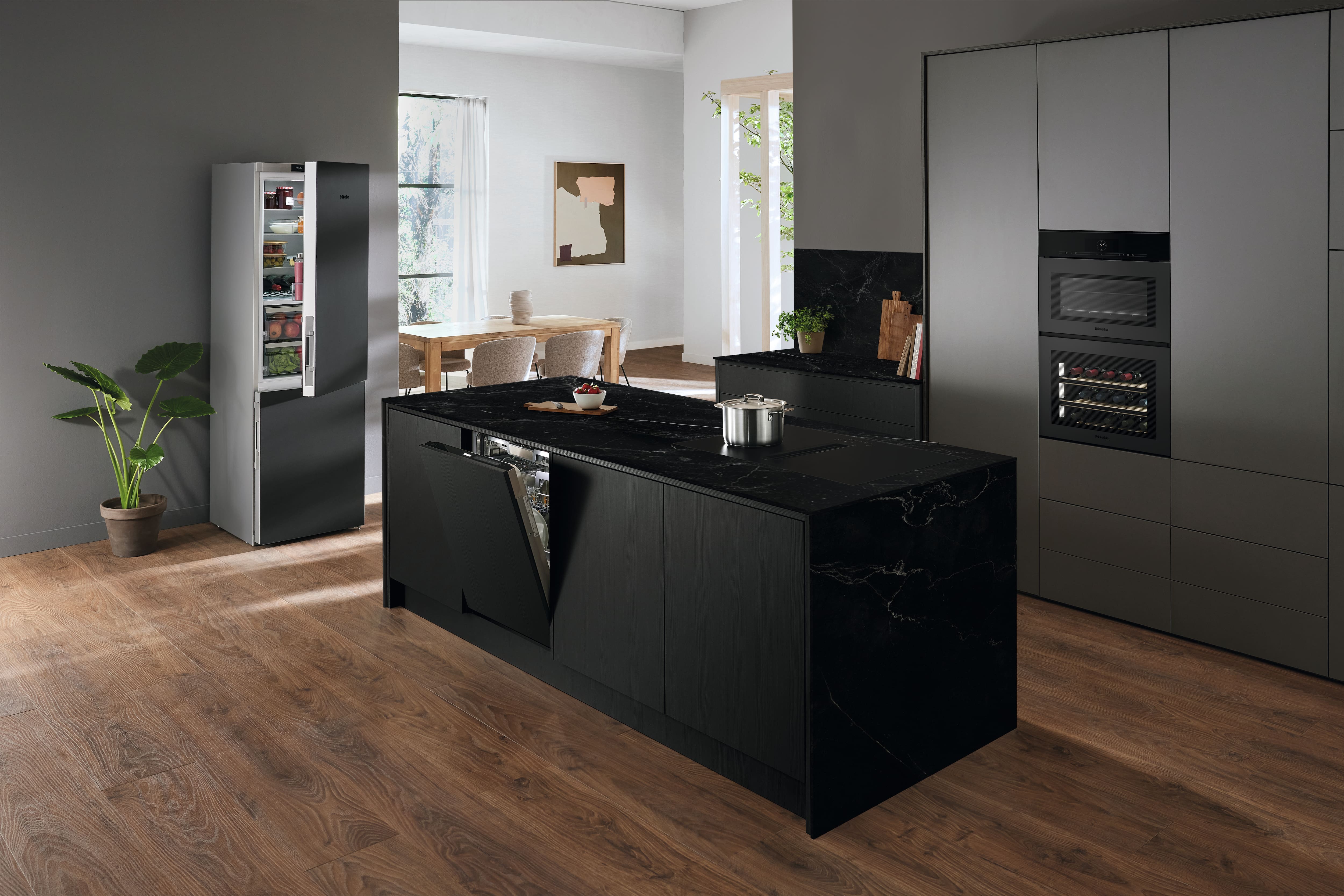 A kitchen featuring Miele appliances in sleek Matt Black design. An active hood is in use, with a pan cooking a meal. In the background, an oven and microwave are visible. A kitchen featuring Miele appliances in sleek Matt Black design. An active hood is in use, with a pan cooking a meal. In the background, an oven and microwave are visible.