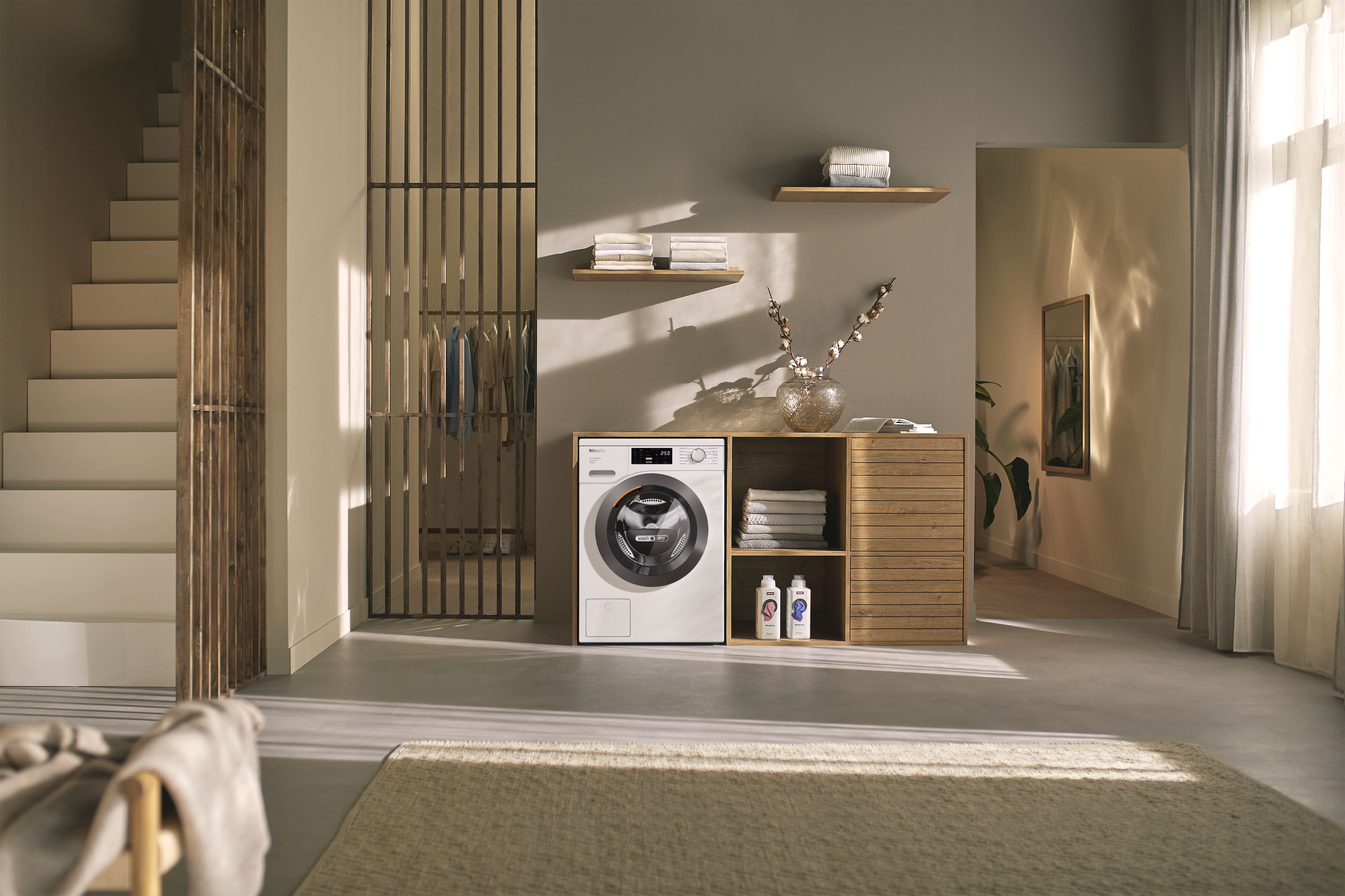 Minimalist laundry nook with front-load washer in wood cabinet, shelves with towels, soft light, and detergents.