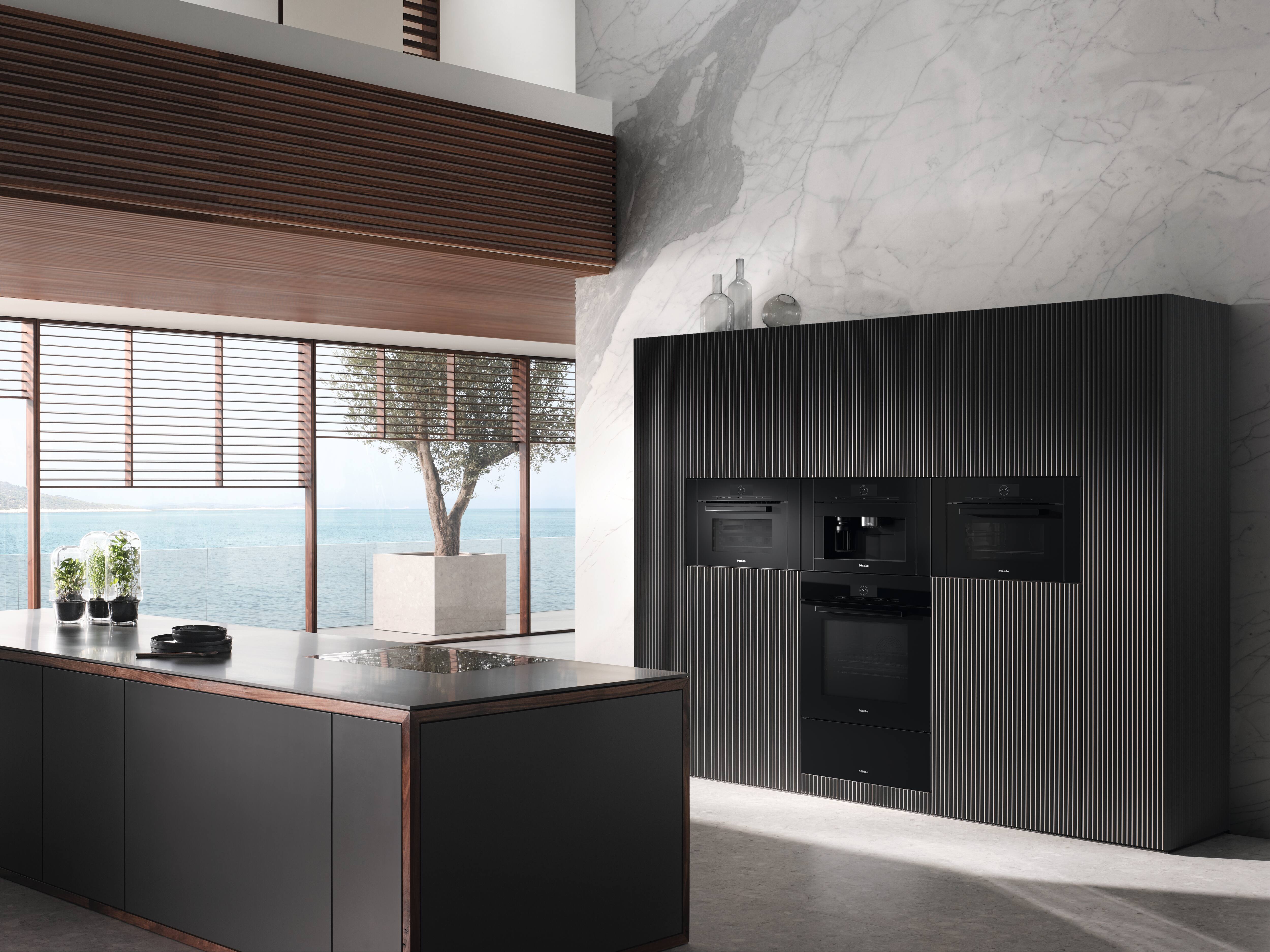 Cozinha minimalista à beira-mar com janelas altas, parede de mármore e eletrodomésticos pretos embutidos ao lado de uma ilha elegante. Cozinha minimalista à beira-mar com janelas altas, parede de mármore e eletrodomésticos pretos embutidos ao lado de uma ilha elegante.
