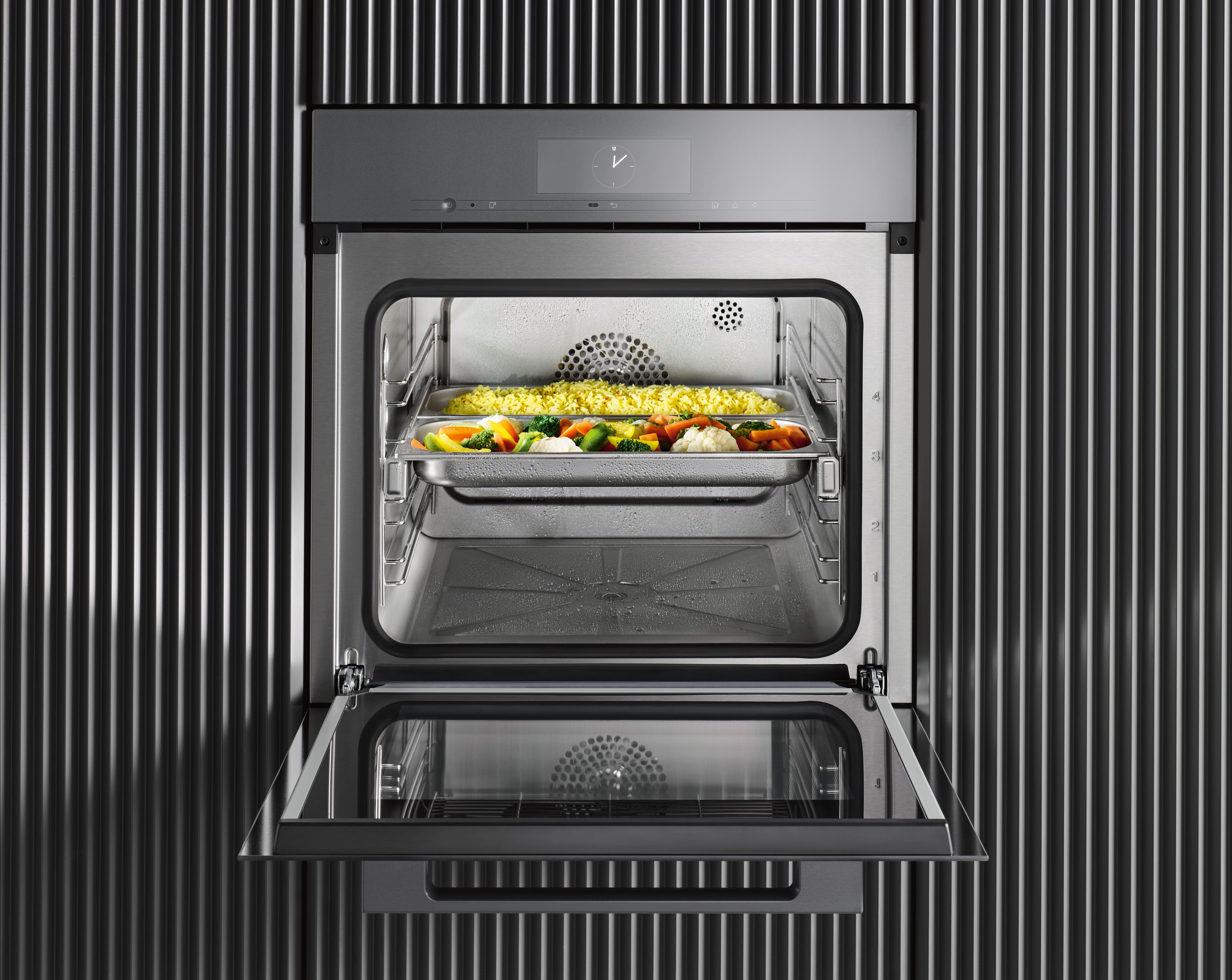 Open stainless steel steam oven with trays of rice and mixed vegetables cooking, showcasing a modern appliance.