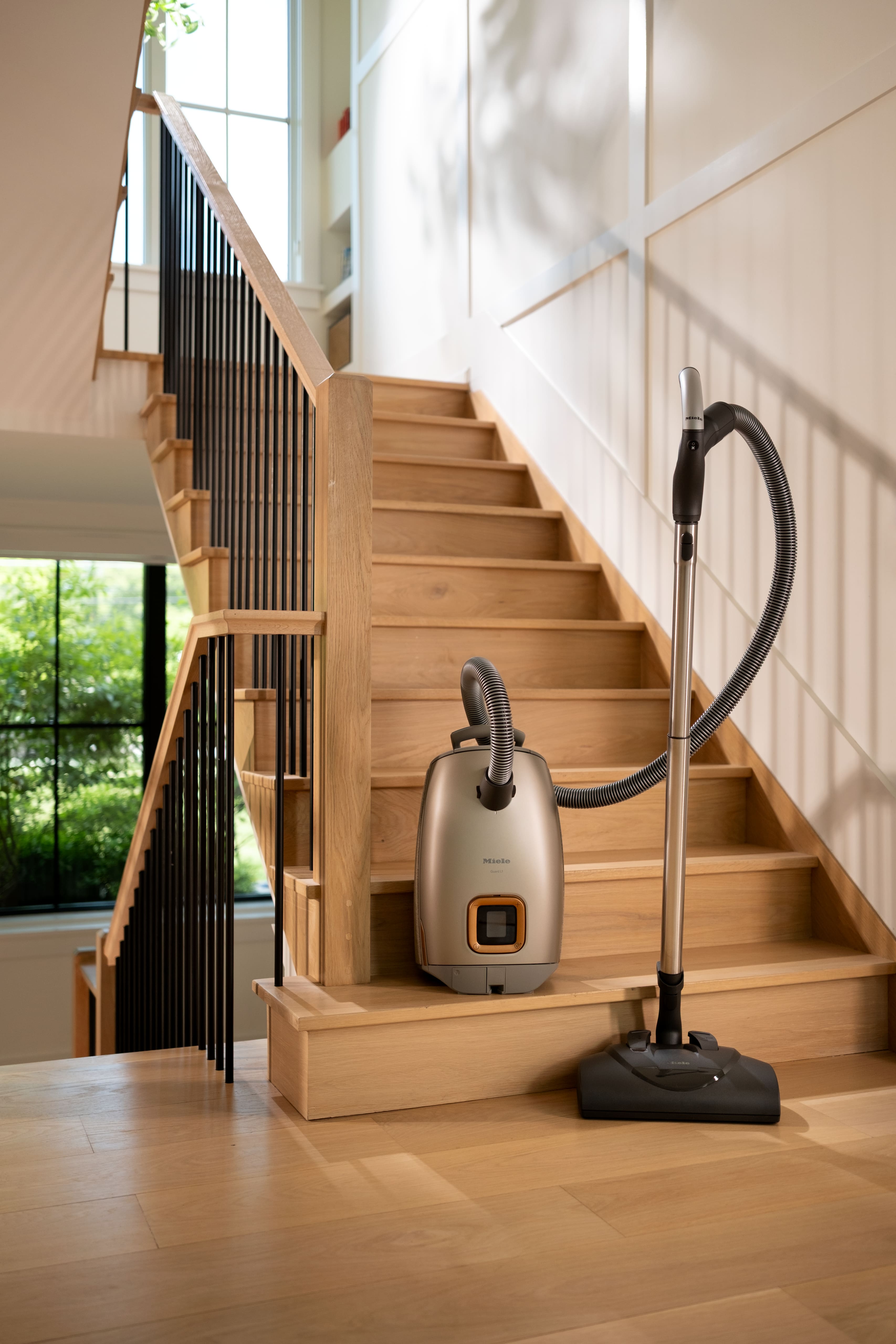 Canister vacuum cleaner on a wooden staircase in a bright, modern home interior with sunlight and large window. Canister vacuum cleaner on a wooden staircase in a bright, modern home interior with sunlight and large window.