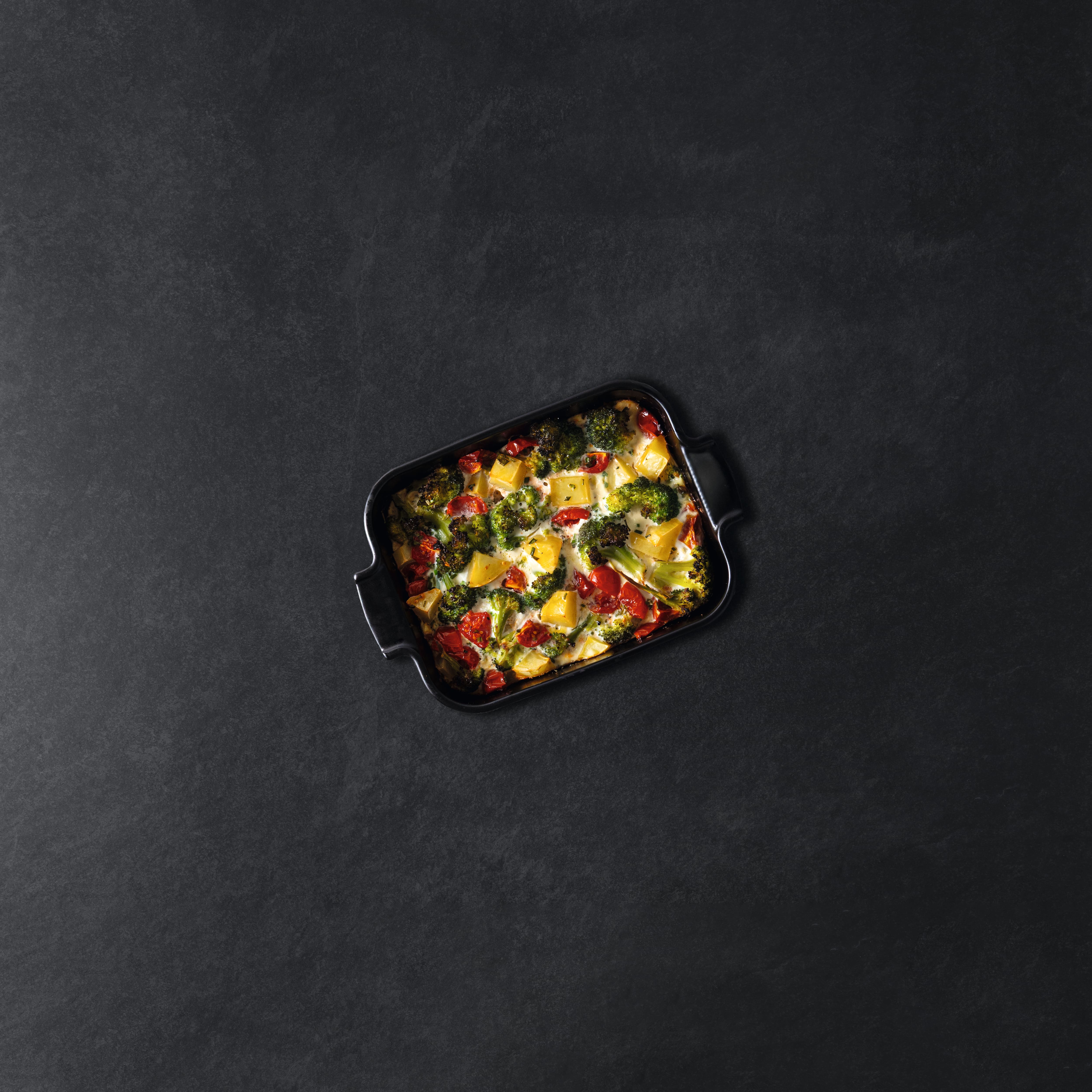 Top-view of a baked vegetable casserole with broccoli, peppers and cheese in a black dish on dark stone. Top-view of a baked vegetable casserole with broccoli, peppers and cheese in a black dish on dark stone.