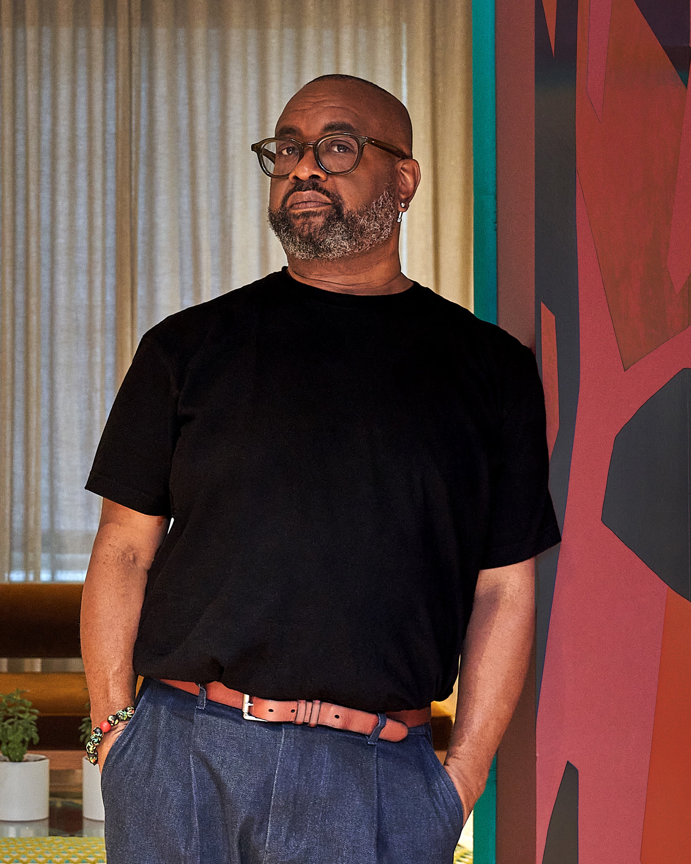 Portrait of a bearded man in black shirt and glasses standing by colorful wall art in a modern room.