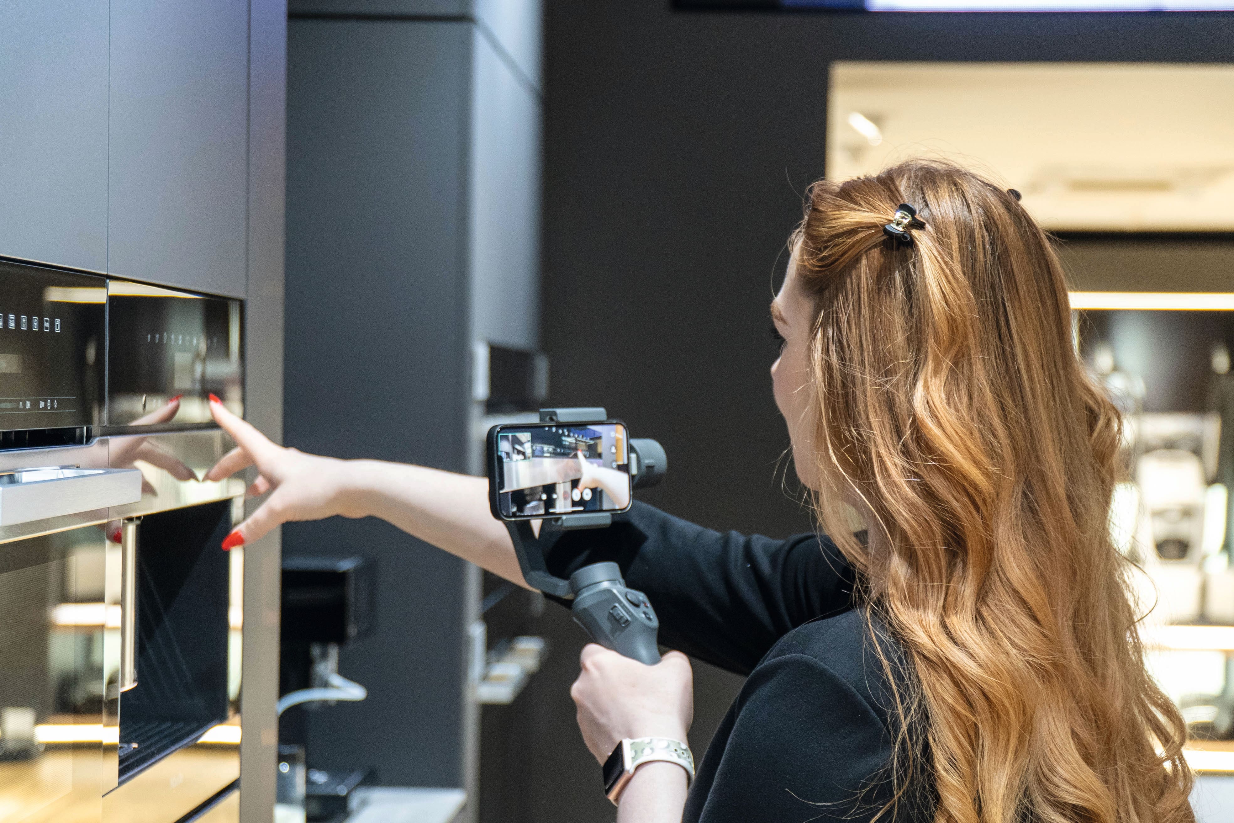 Person filmer et moderne køkkenapparat med en smartphone på en gimbal, peger på touch kontrolpanelet.