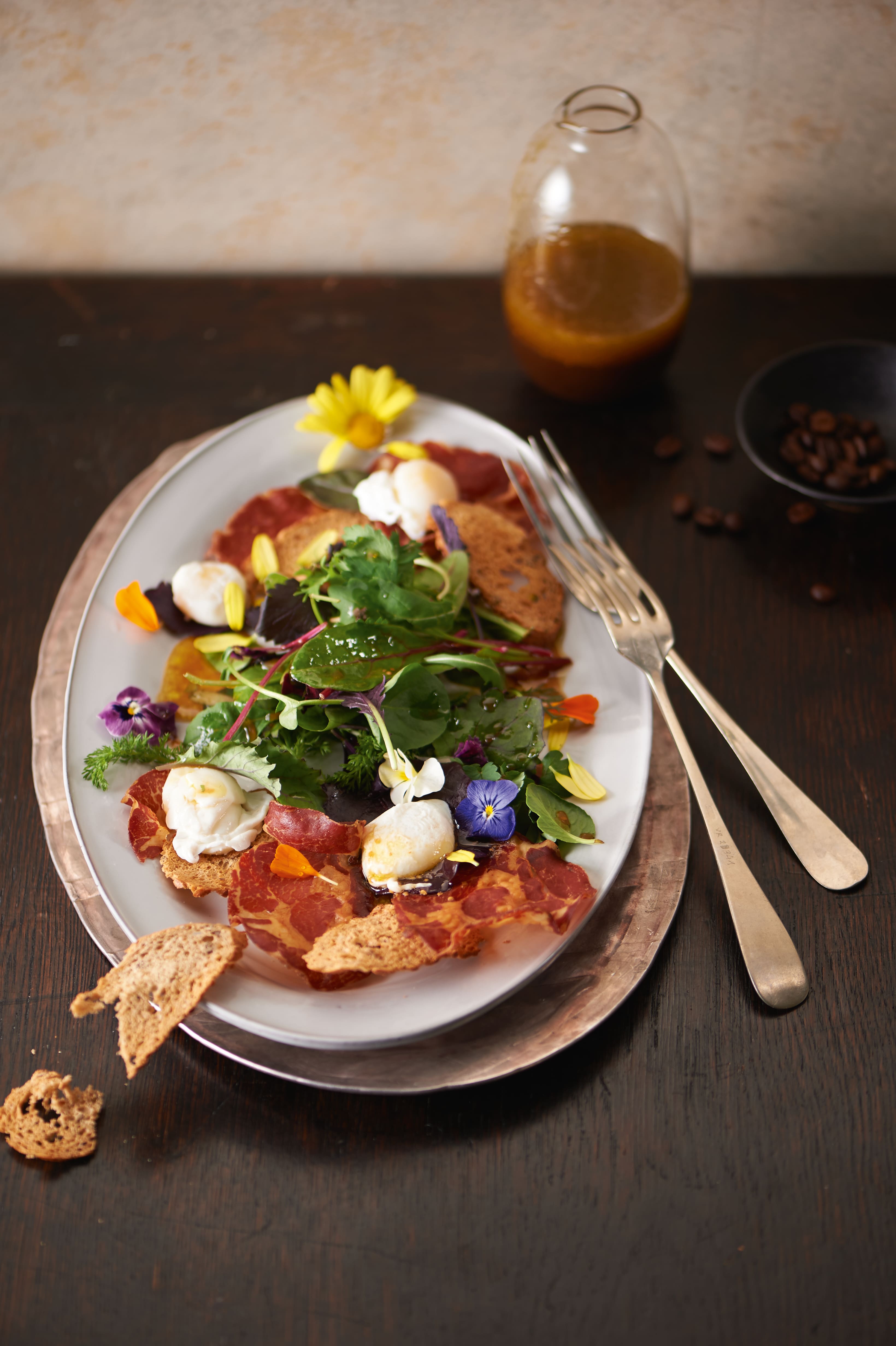 Gourmet salad with cured meat, greens, edible flowers, and croutons, served with vinaigrette on table. Gourmet salad with cured meat, greens, edible flowers, and croutons, served with vinaigrette on table.