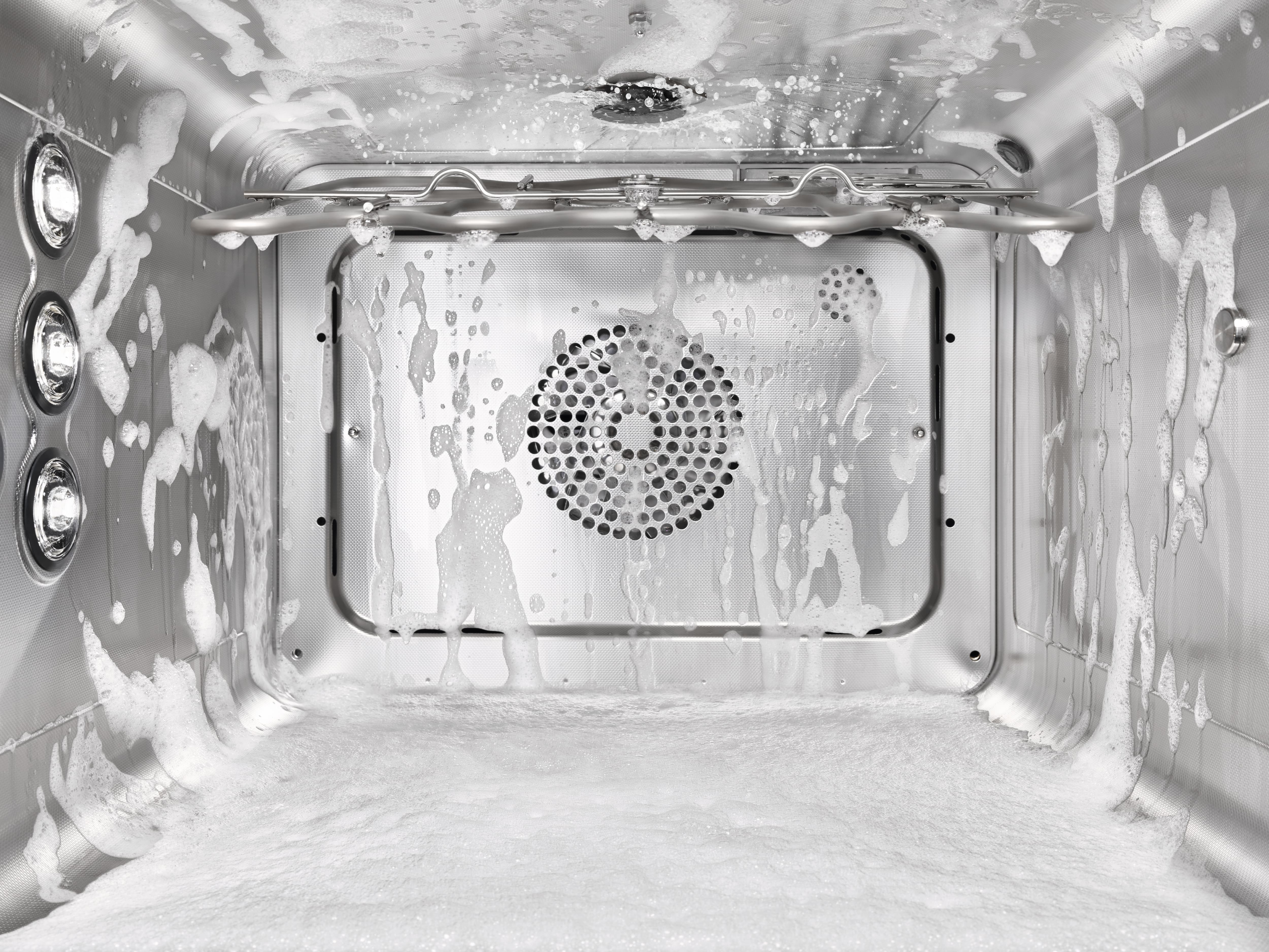 Stainless-steel convection oven interior during a cleaning cycle, with soap foam coating the walls and floor. Stainless-steel convection oven interior during a cleaning cycle, with soap foam coating the walls and floor.