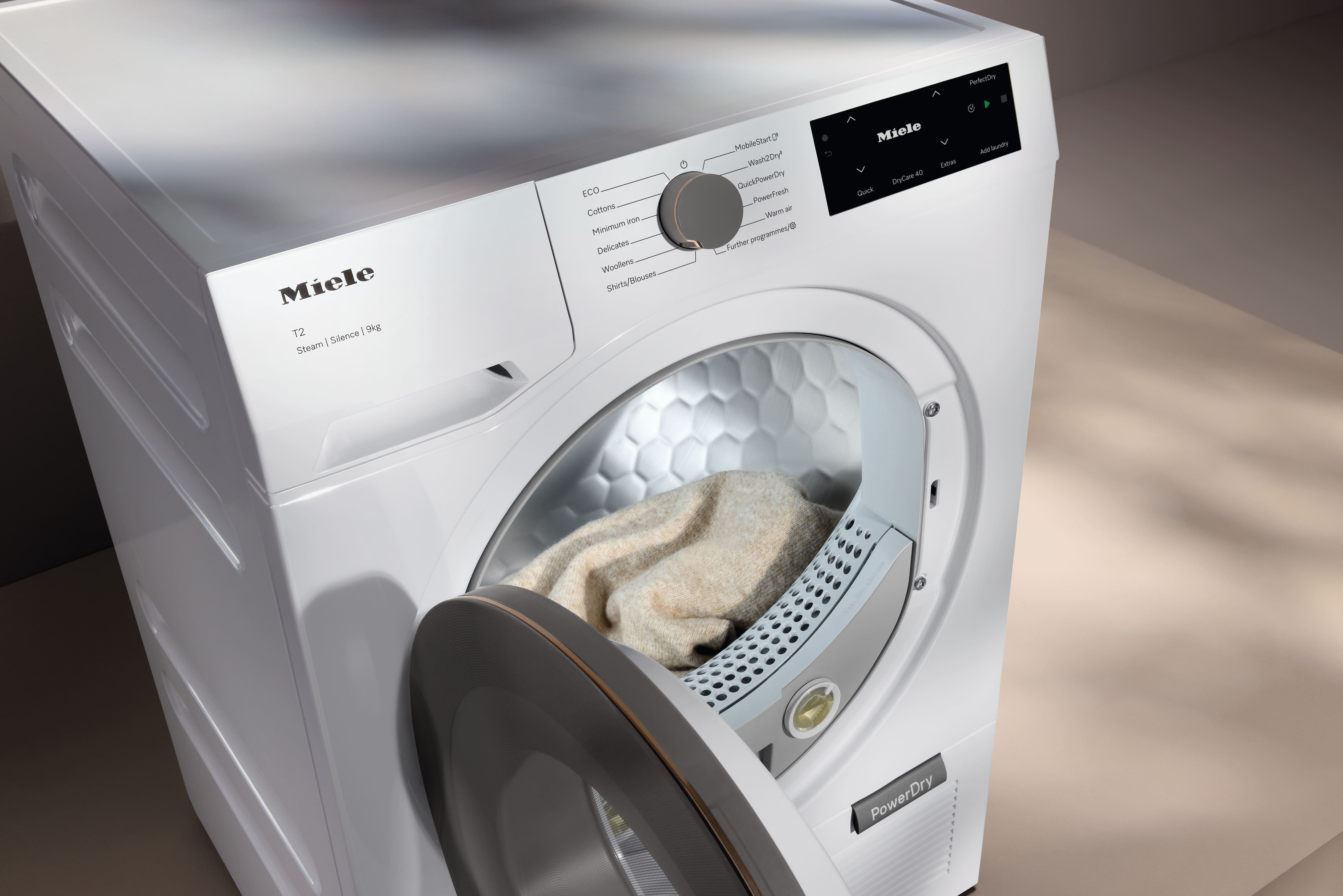 白色 Miele T2 PowerDry 乾衣機，門打開，蜂巢狀滾筒內有一件羊毛衫，可以看到控制面板。