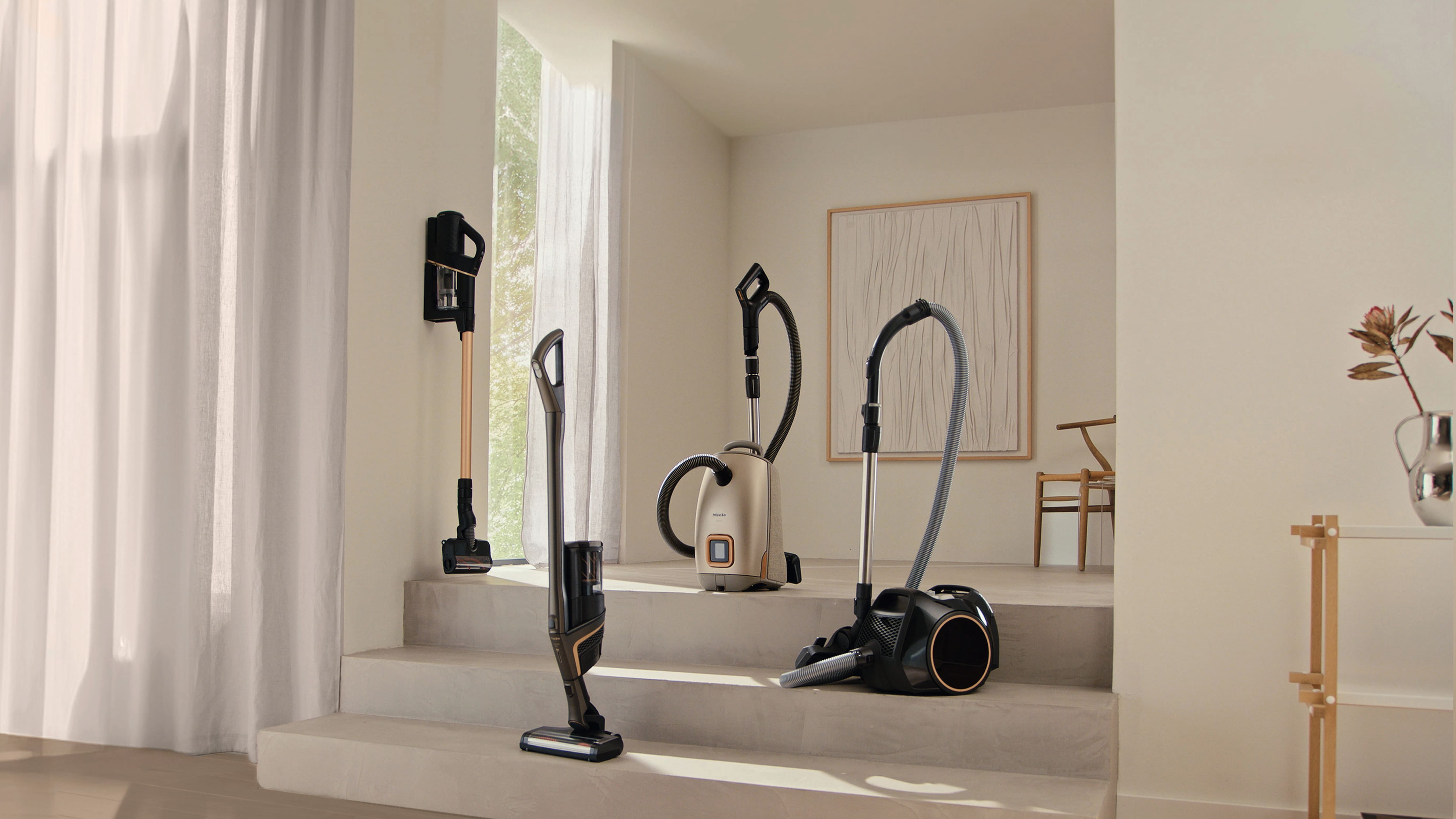 Intérieur moderne mettant en valeur plusieurs aspirateurs Miele, modèles balais et traîneaux, disposés sur des marches à des fins de présentation.