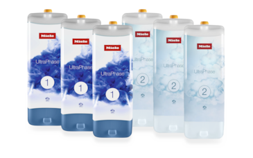 Set 6 UltraPhase - Miele UltraPhase 1 ve 2 Altı Miele UltraPhase deterjan kartuşu - üçü "1" ve üçü "2" etiketli - Side-by-Side duran, mavi sıvı grafikli ve sarı kapaklı beyaz dikdörtgen şişeler.