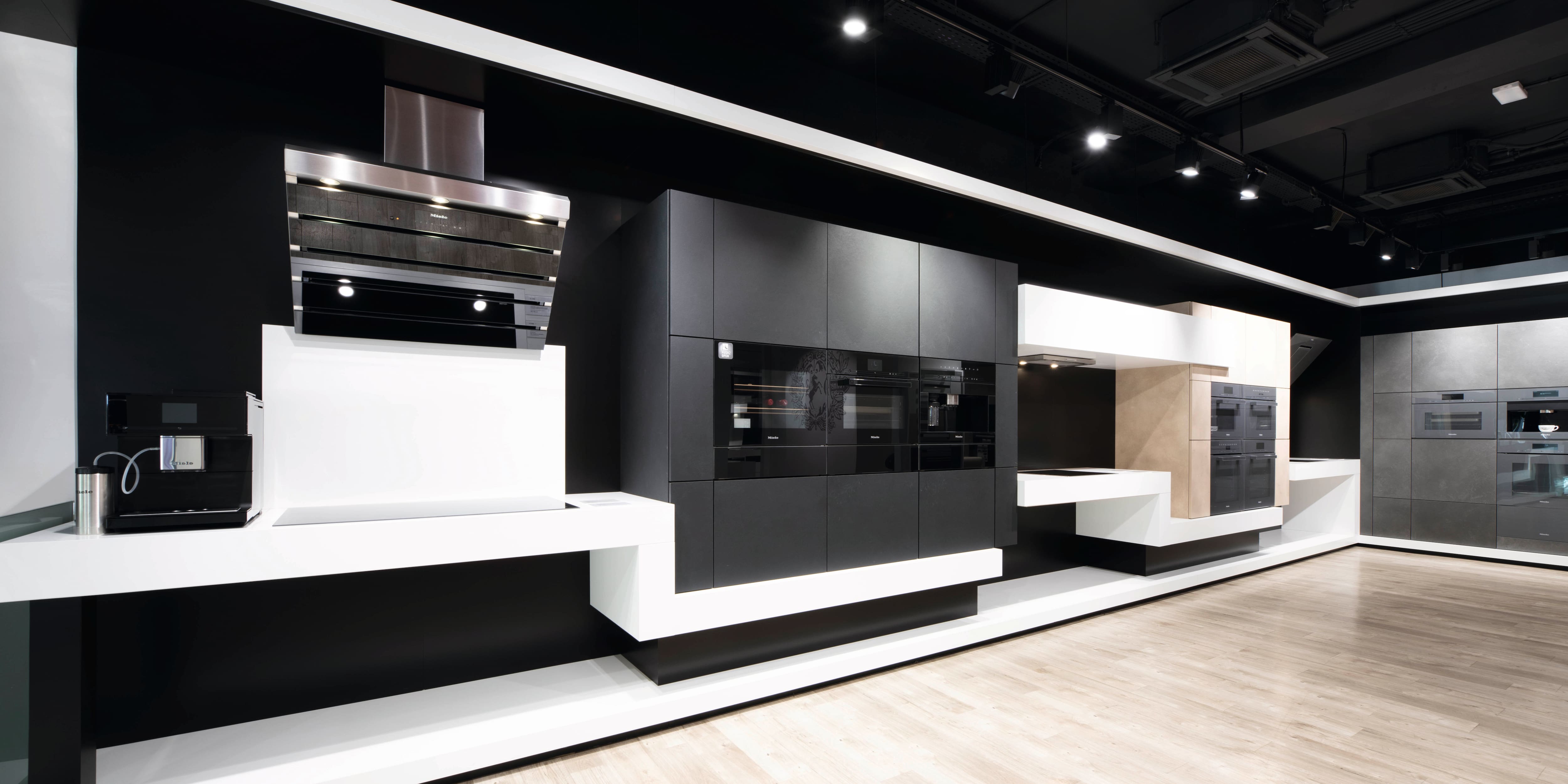 Moderno showroom con elegantes electrodomésticos de cocina integrados en gabinetes negros, plataformas blancas y suelo de madera. Moderno showroom con elegantes electrodomésticos de cocina integrados en gabinetes negros, plataformas blancas y suelo de madera.