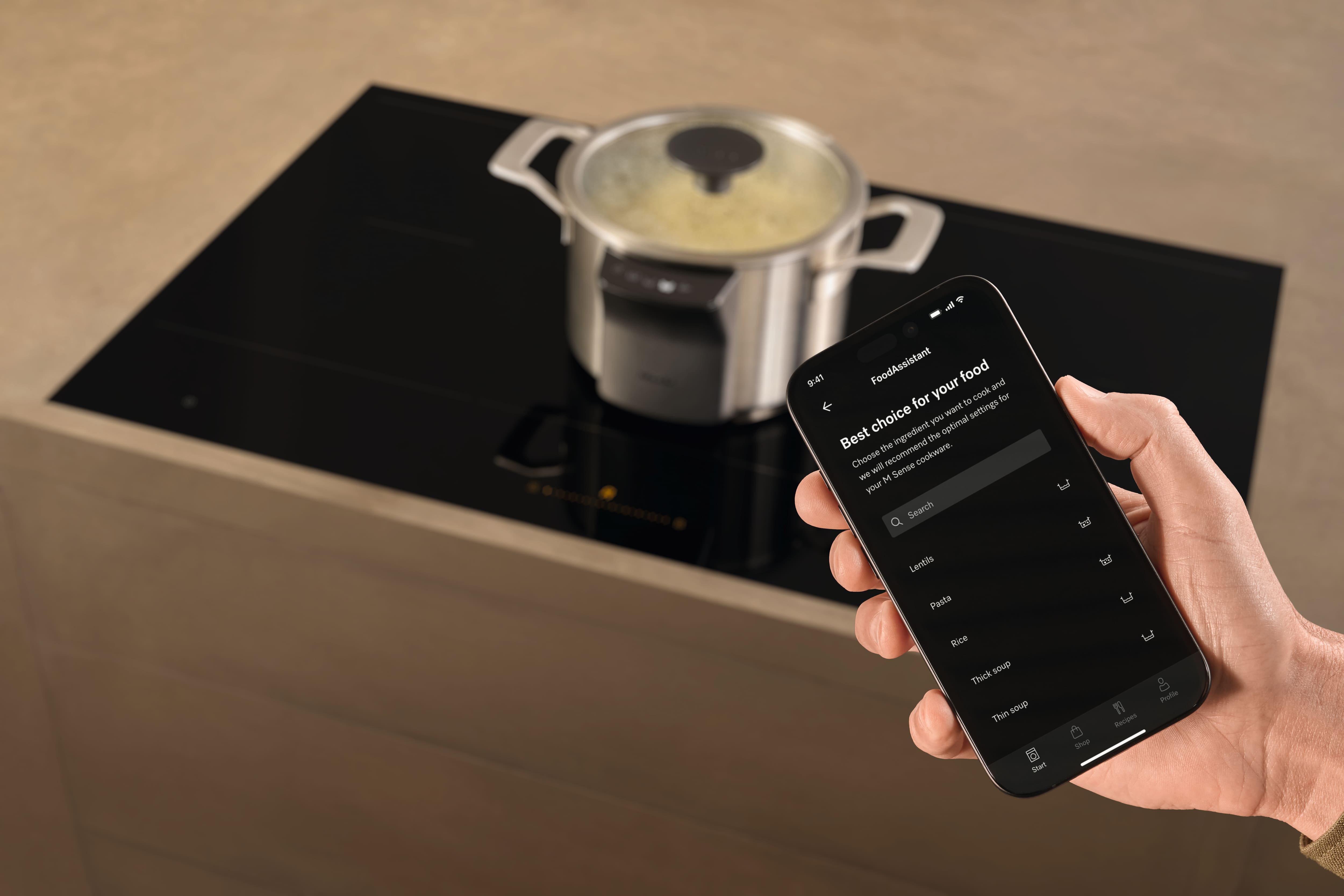 Hand holding phone with cooking app controls beside pan searing two steaks on an induction cooktop. Hand holding phone with cooking app controls beside pan searing two steaks on an induction cooktop.