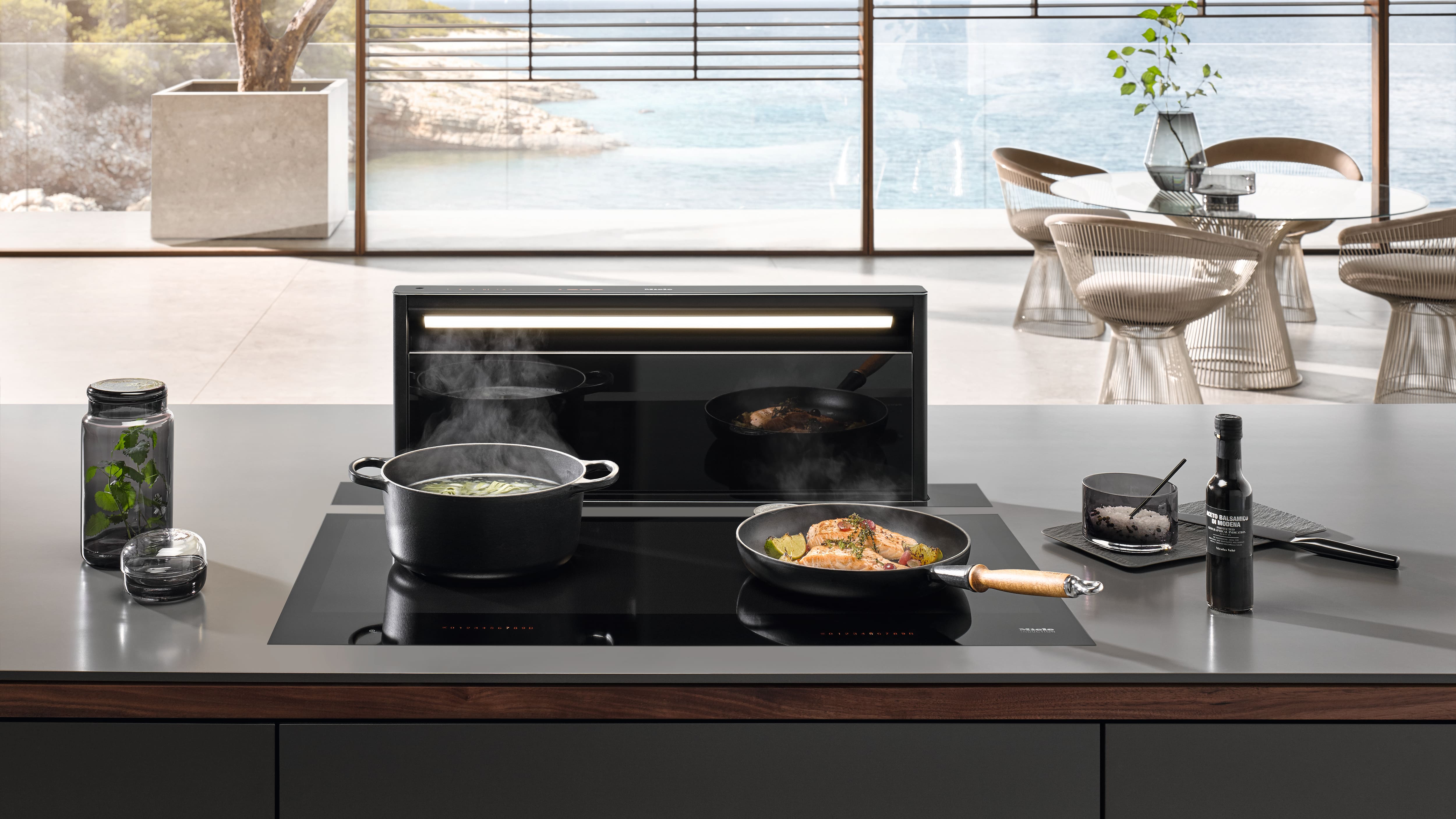 Modern kitchen island with induction cooktop and pop-up downdraft hood, pans cooking veggies with steam. Modern kitchen island with induction cooktop and pop-up downdraft hood, pans cooking veggies with steam.