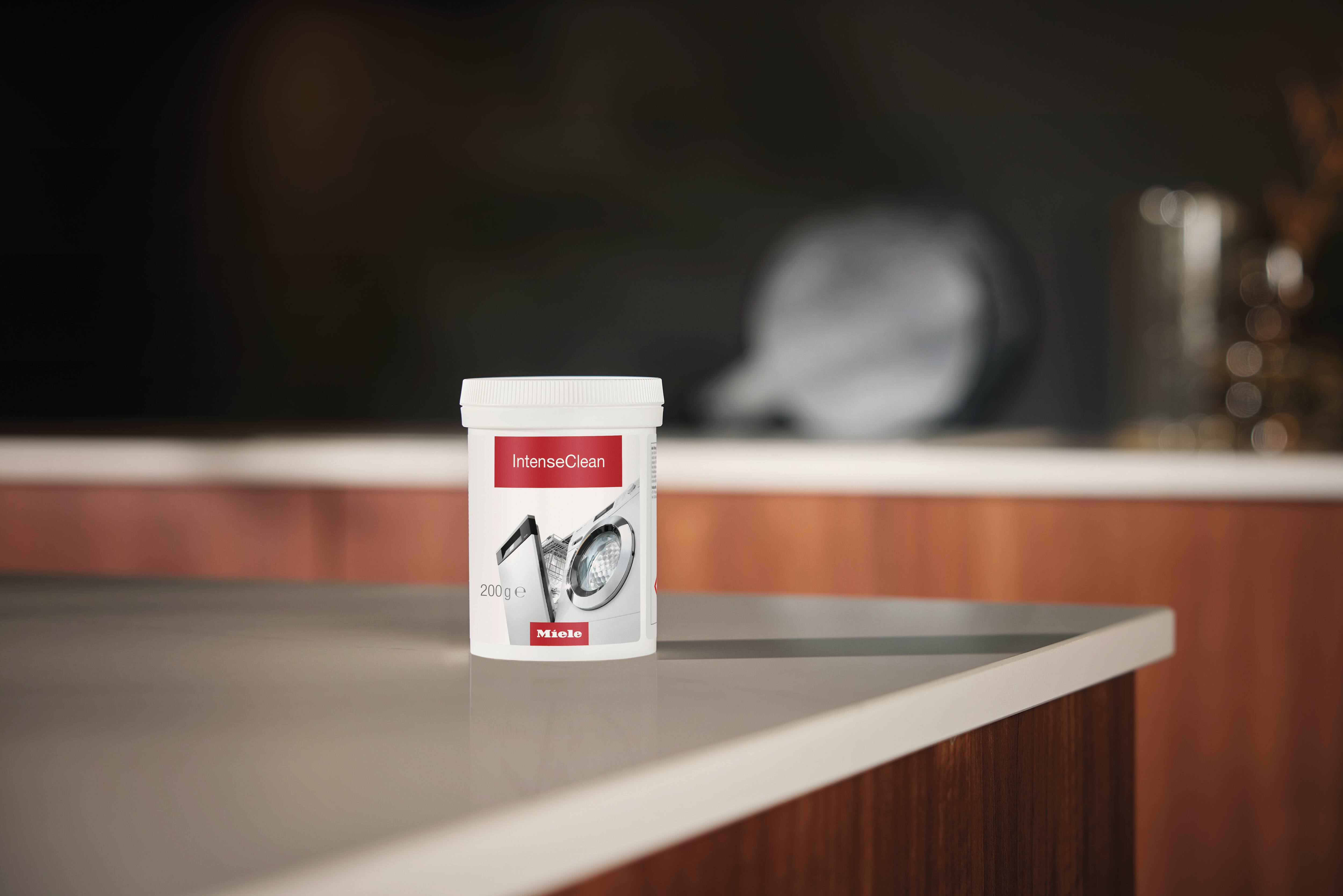 Um pote de plástico branco com a etiqueta “IntenseClean” (200 g) da Miele está sobre a bancada de uma cozinha moderna, com um fundo desfocado. Um pote de plástico branco com a etiqueta “IntenseClean” (200 g) da Miele está sobre a bancada de uma cozinha moderna, com um fundo desfocado.