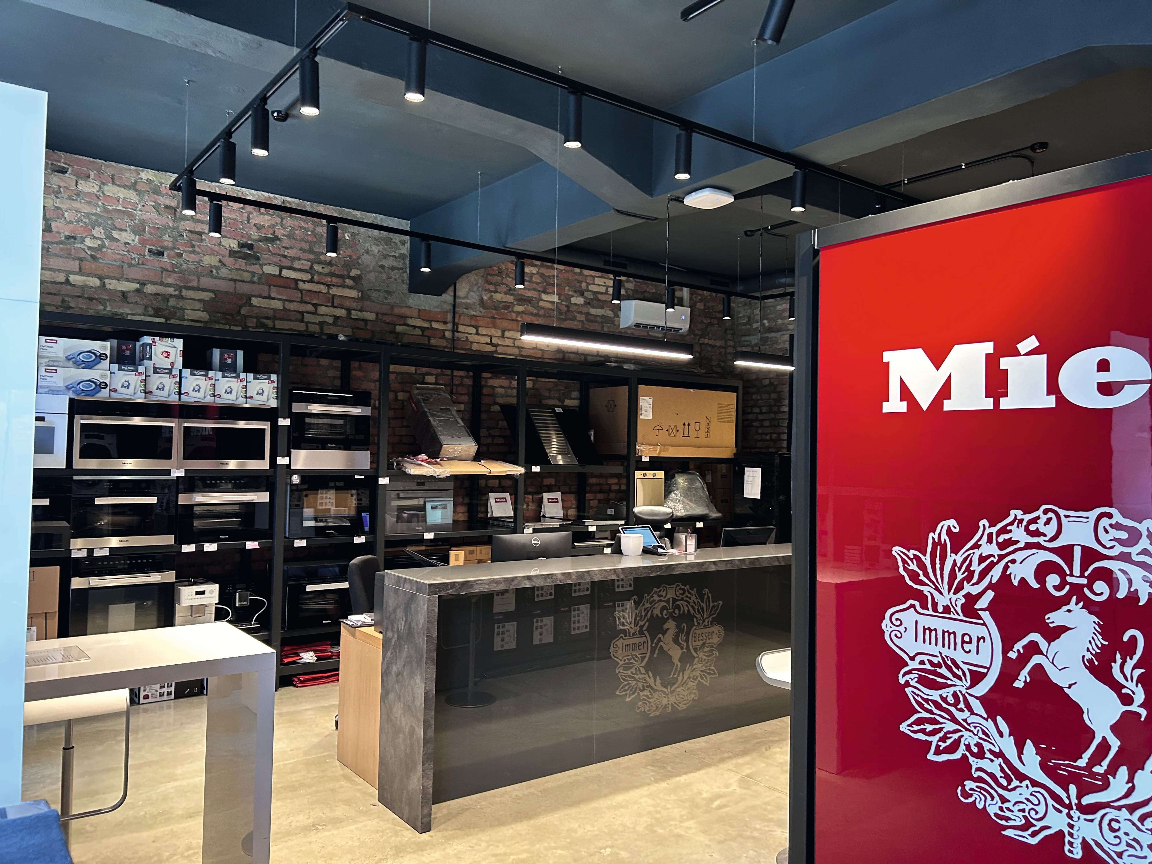 Mūsdienīgs sadzīves tehnikas salons ar Miele zīmolu, ķieģeļu siena, sliežu apgaismojums un plaukti ar iebūvētām krāsnīm. Mūsdienīgs sadzīves tehnikas salons ar Miele zīmolu, ķieģeļu siena, sliežu apgaismojums un plaukti ar iebūvētām krāsnīm.