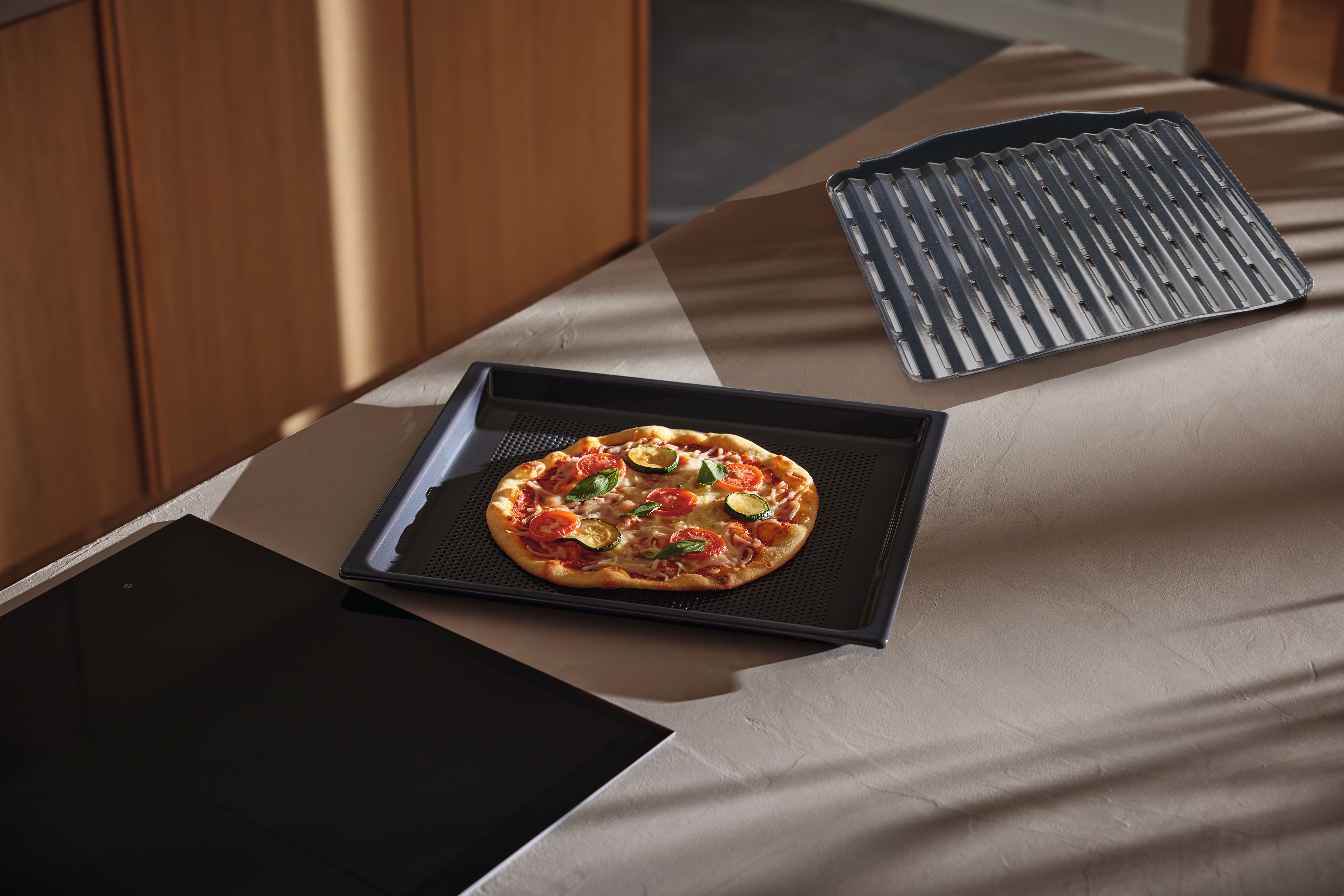 Świeżo upieczona pizza wegetariańska na perforowanej blasze do pieczenia Miele, stojącej na blacie kuchennym, a obok niej blacha do grillowania Miele.
