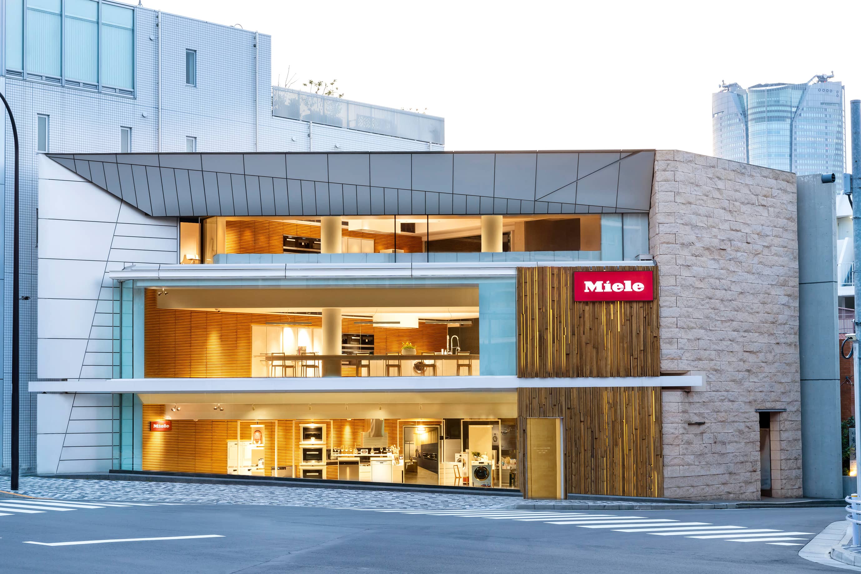 日本:ガラスのファサードを持つモダンな3階建てのミーレショールームで、各階にキッチン家電やインテリアが展示されています。 日本:ガラスのファサードを持つモダンな3階建てのミーレショールームで、各階にキッチン家電やインテリアが展示されています。