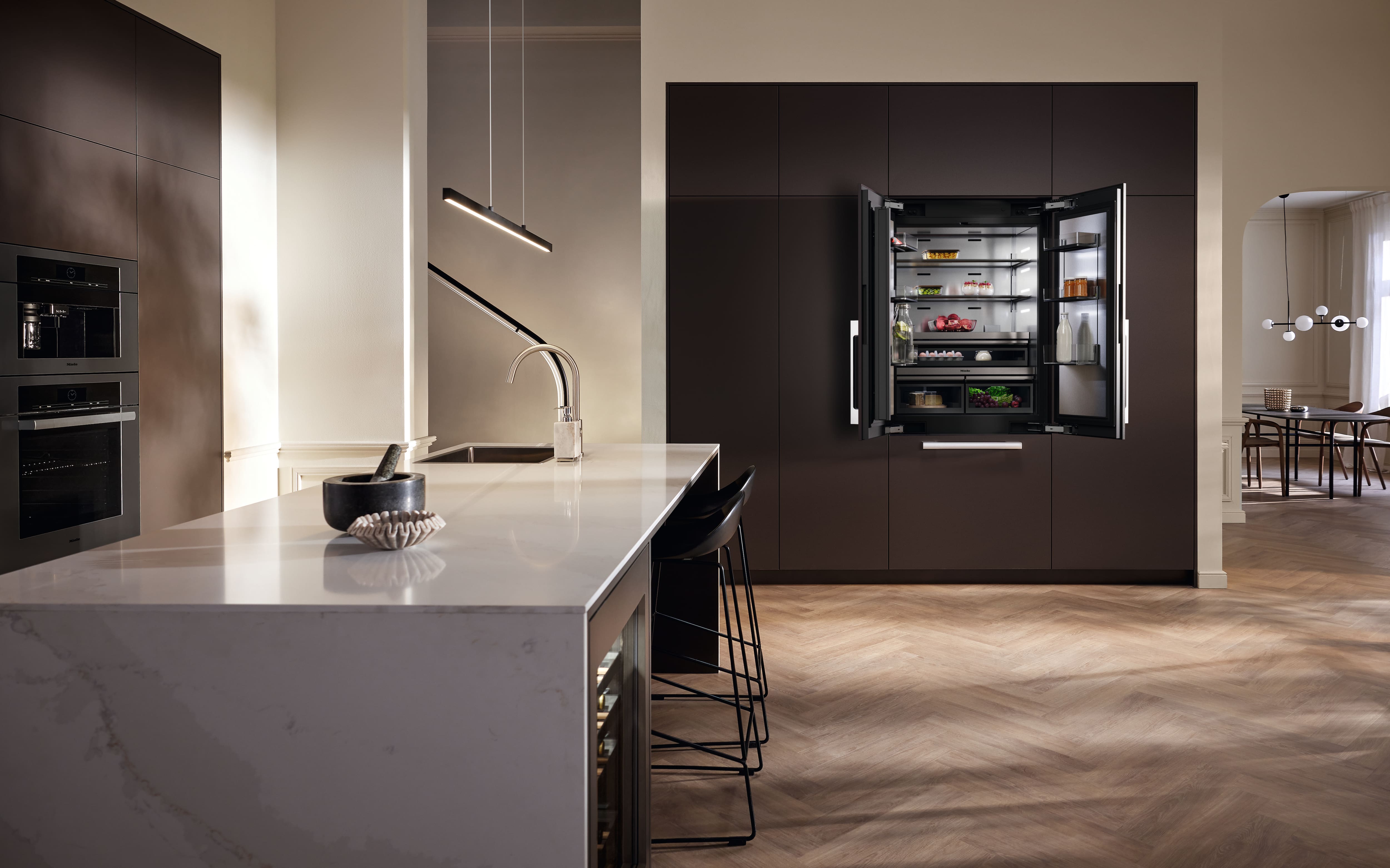 Modern kitchen with island, pendant lighting, and an open built-in French-door fridge amid sleek dark cabinetry.