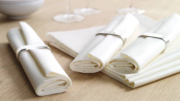 Trois serviettes enroulées dans des ronds de serviette placées sur une table