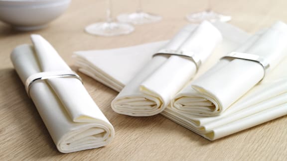 Tre rullade servetter i servettringar ligger på ett bord