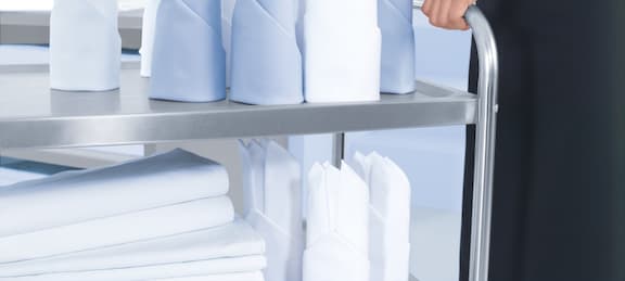 Hands move a serving trolley with folded blue and white napkins.
