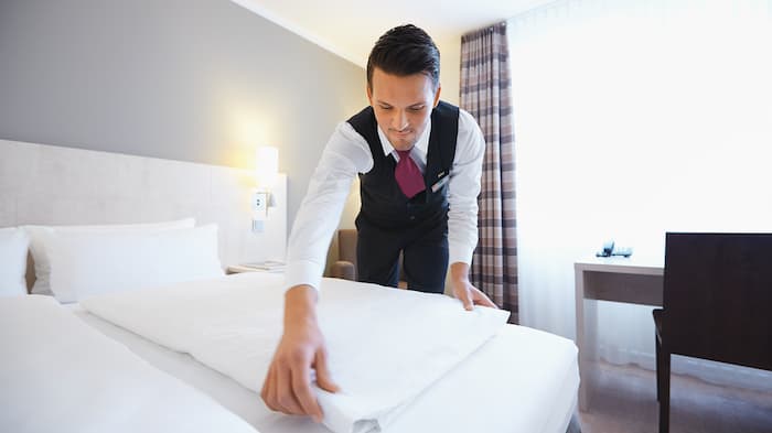 Un valet de chambre dépose des serviettes d’une propreté éclatante sur le lit d’une chambre d’hôtel