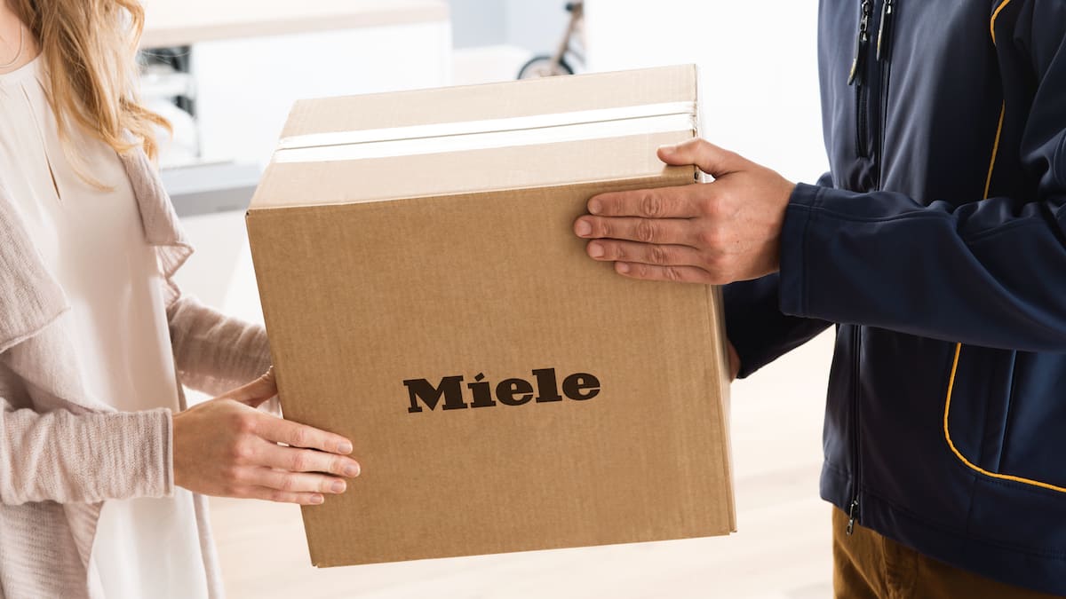 Paket mit Ersatzteilen wird durch Postboten an Empfängerin überreicht