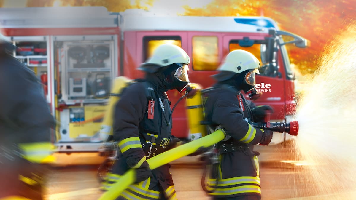 Zwei Feuerwehrmänner löschen Feuer mit Wasserschlauch.