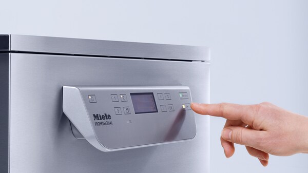 Hand bedient gewerbliche Spülmaschine von Miele Professional am Display.