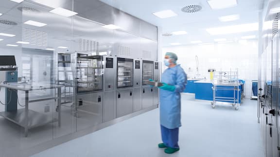 Employee in hospital clothing stands in front of a row of grey reprocessing machines.