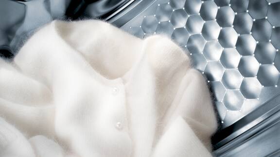 En hvid uld-pullover ligger i en vasketromle