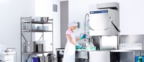 Service employee operates a professional throughfeed dishwasher from Miele.