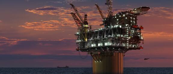 Osvětlená ropná plošina stojí v moři před rudým nebem.
