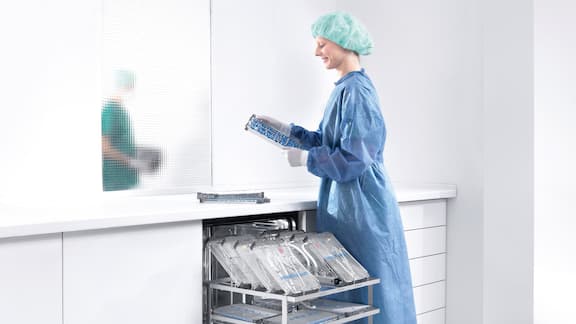 Leikkaussalivaatteisiin pukeutunut hoitaja täyttämässä Miele Professional ‑pesu- ja desinfiointikonetta.