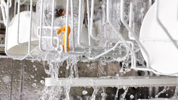 View into the inner cabinet of a dishwasher with turning spray arms, water drops and cutlery. 